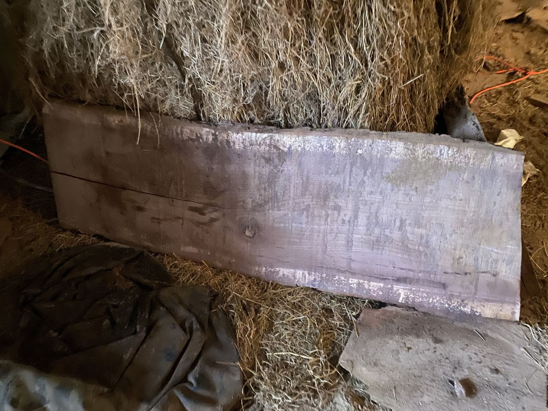 A weathered wooden beam rests on hay in a barn.