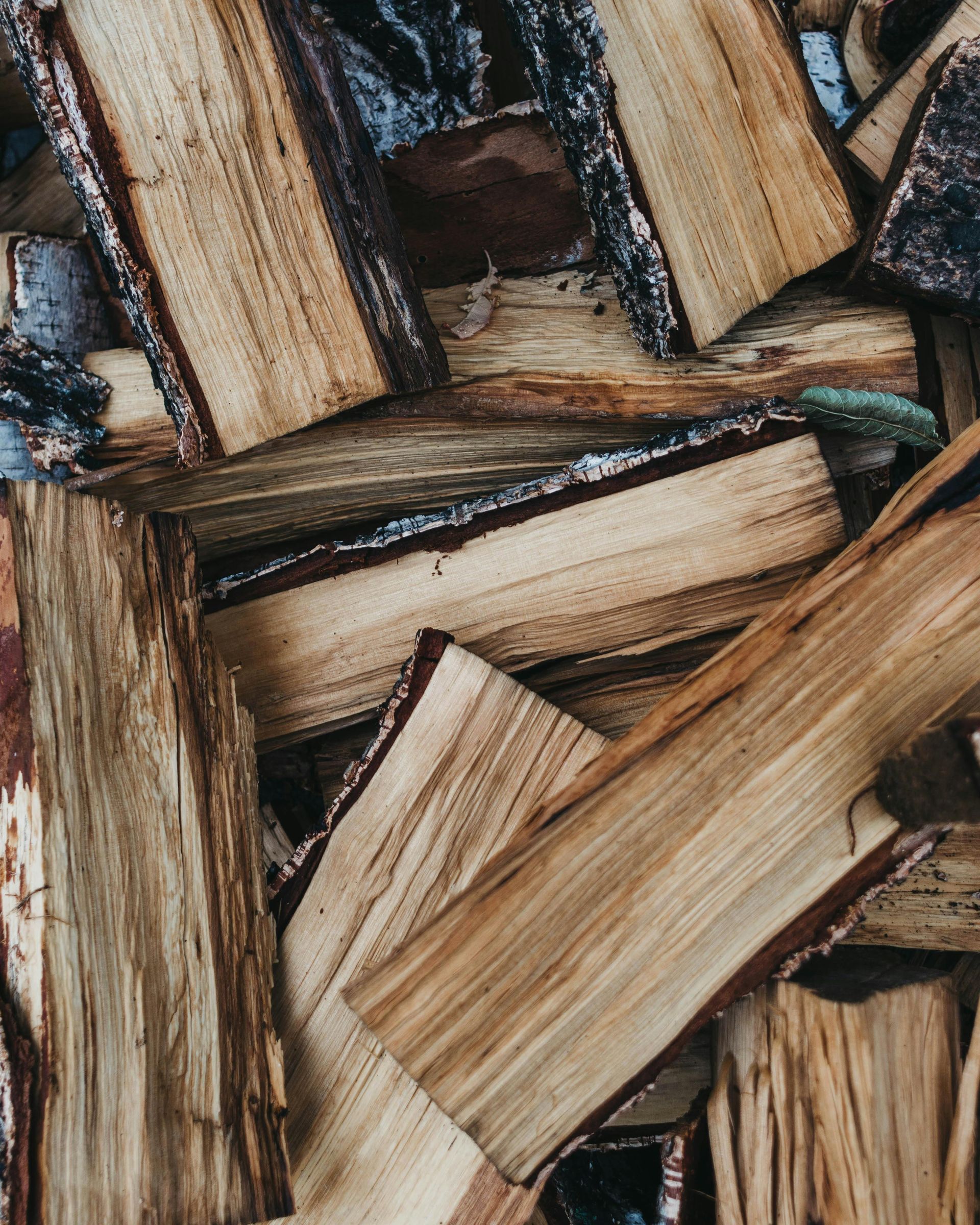 Pile of split firewood, mostly light brown, with dark bark edges, ready for burning.