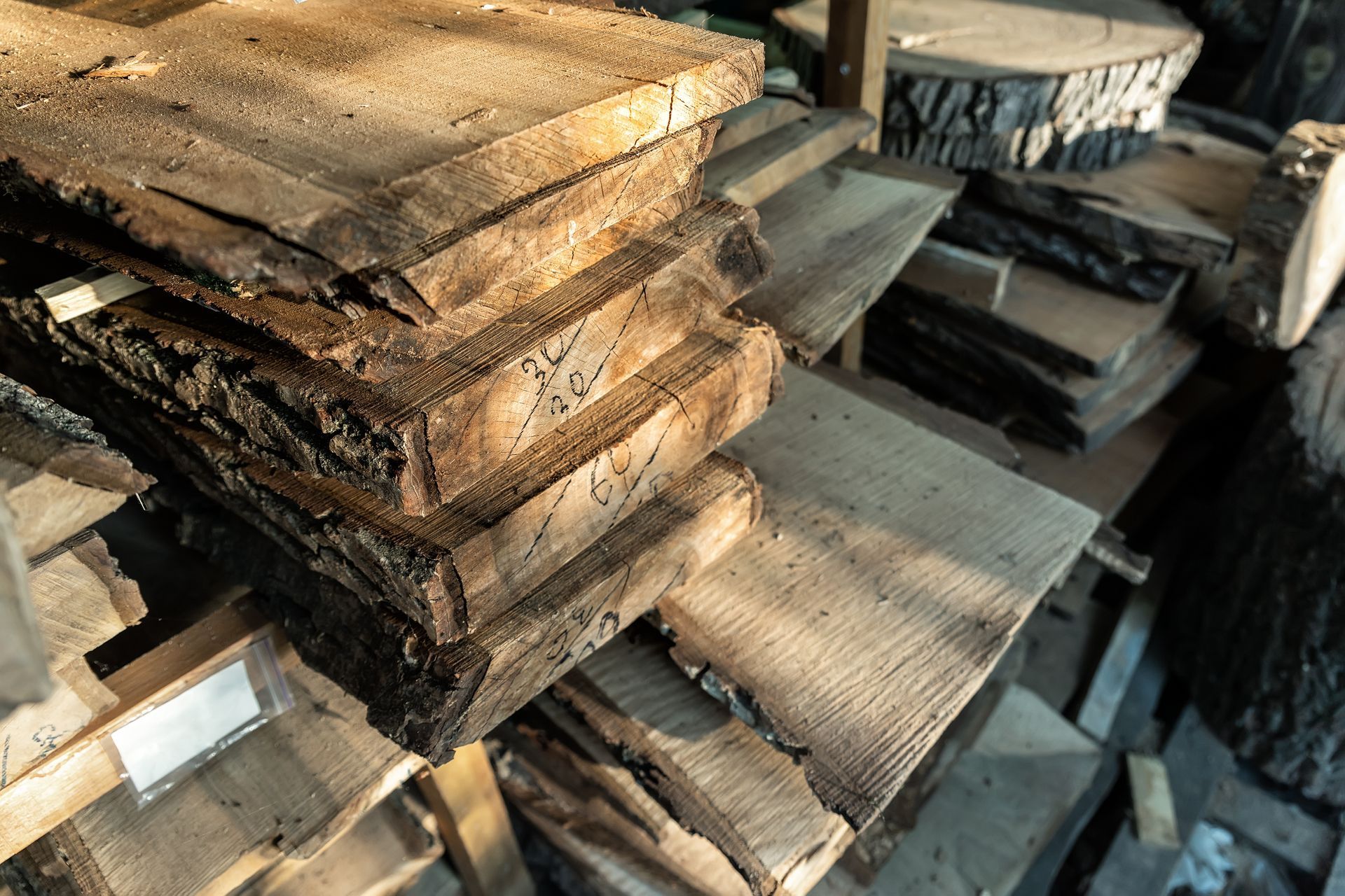 Stack of rough-hewn wooden slabs in a workshop, exposed to sunlight.