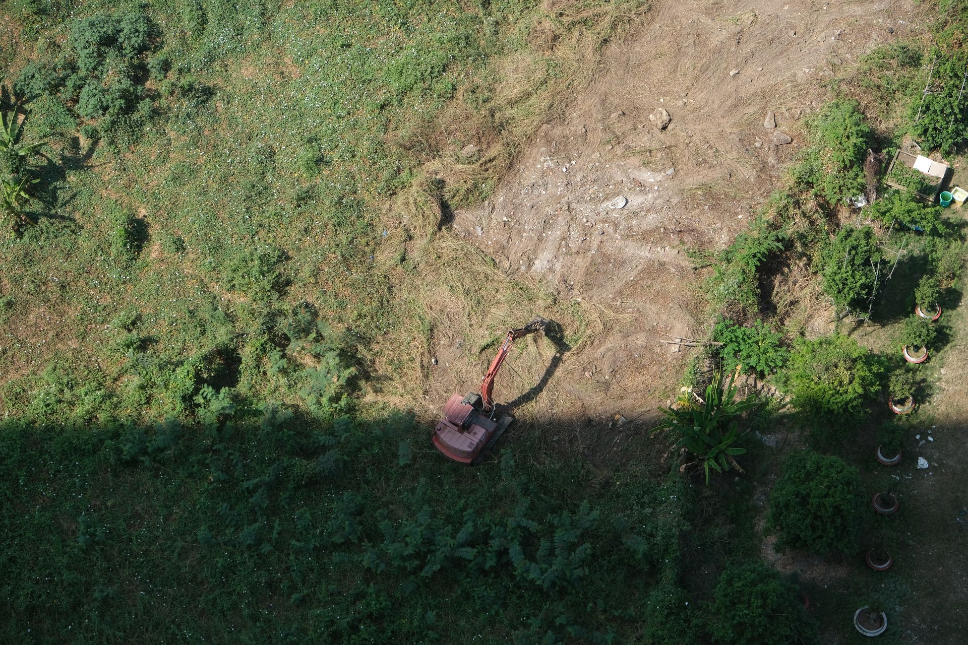 Top-down view of an excavator on brown dirt and green grass.