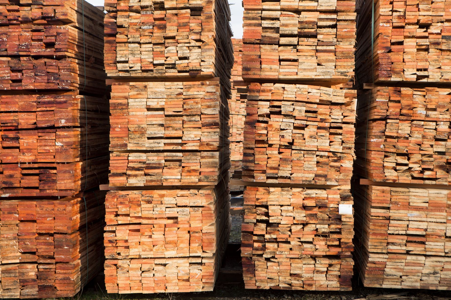 Stacks of reddish-brown lumber planks, arranged in neat piles at a lumber yard.