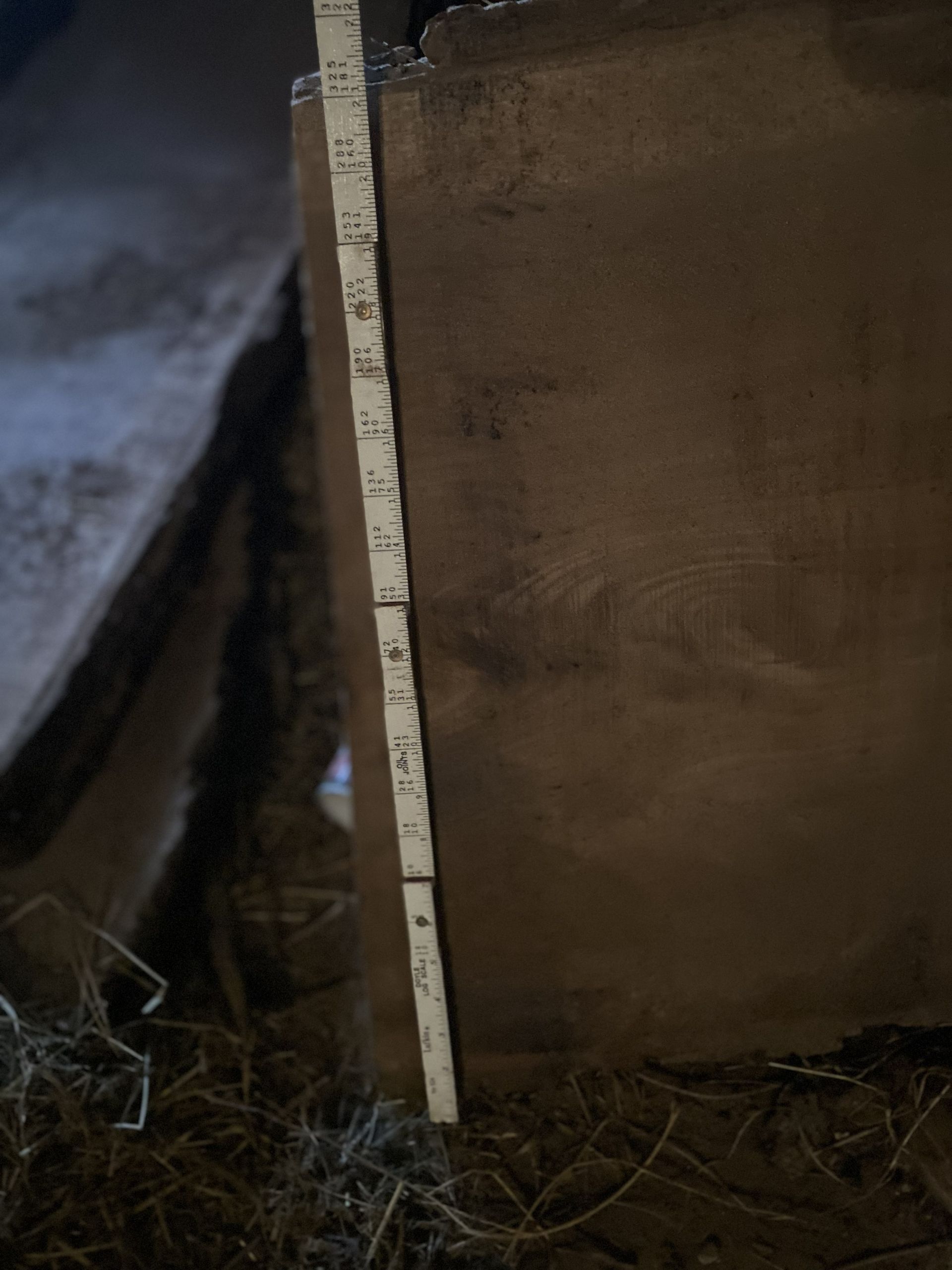 A wooden ruler next to a brown surface, possibly measuring it. Dark setting.