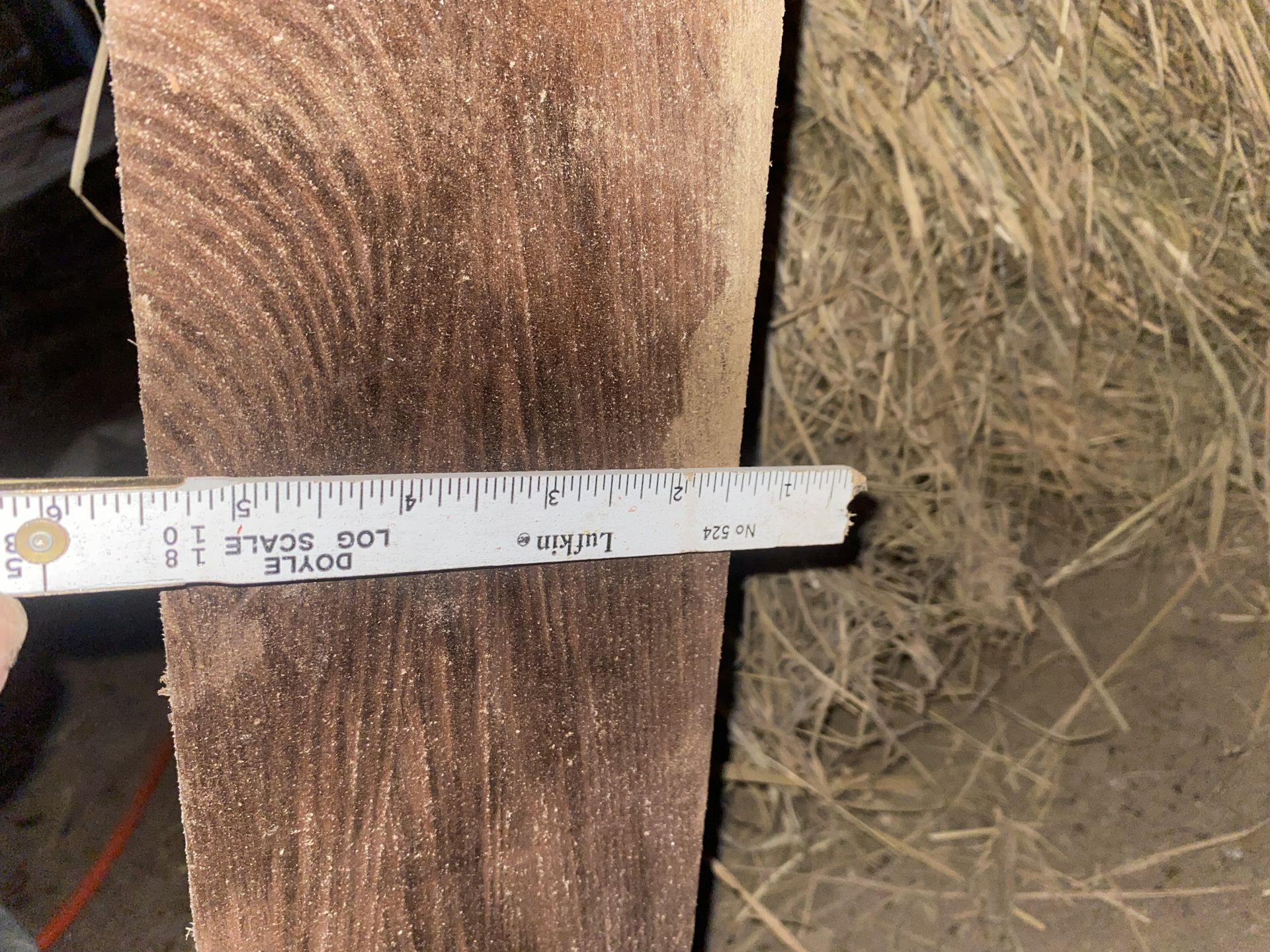 Wooden beam being measured with a ruler against a backdrop of hay and dirt.