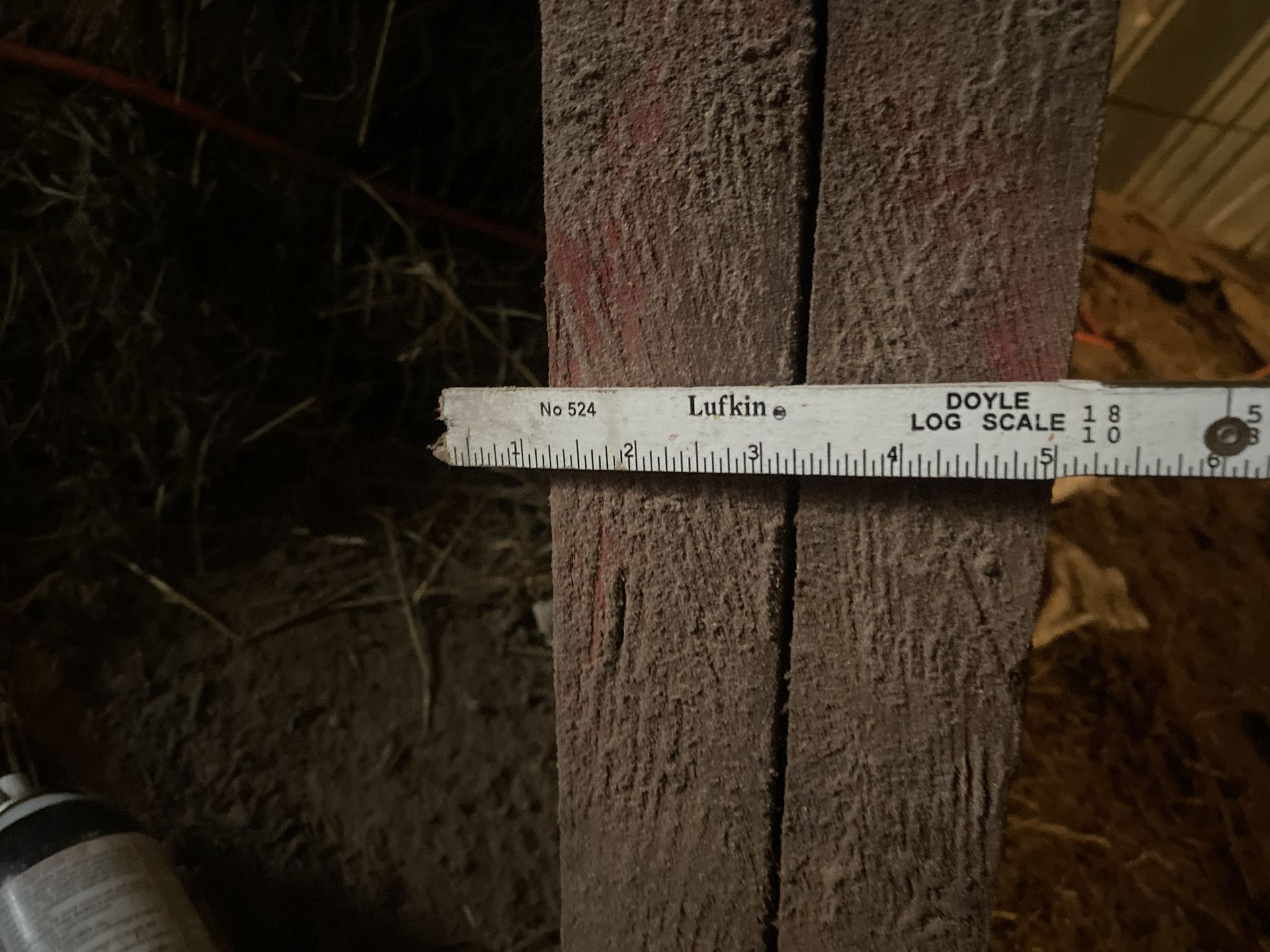 A ruler measuring a gap between two weathered wooden planks in a dim setting.