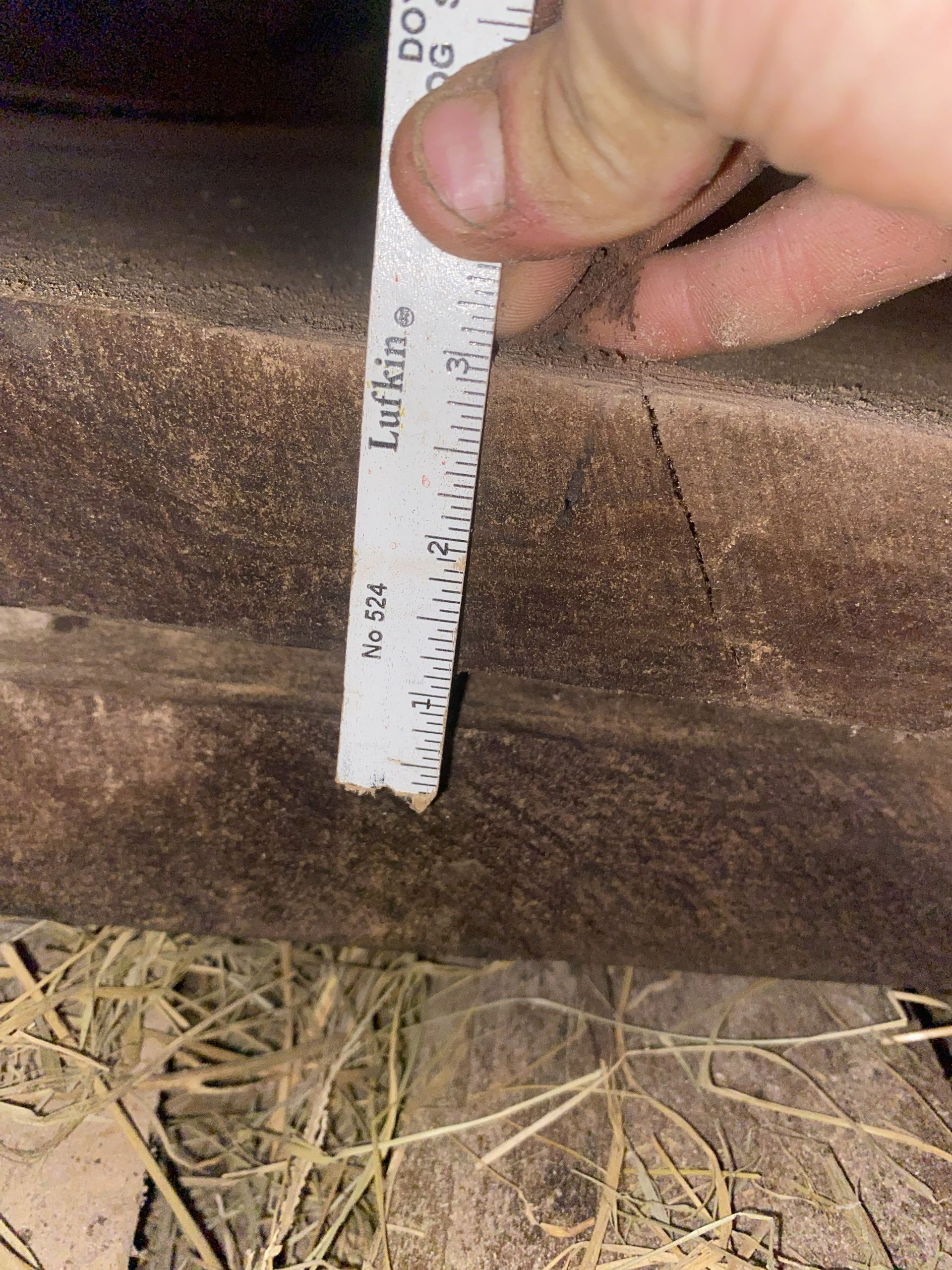 Hand holding a ruler, measuring a brown, wooden surface. The measurement is about 1/2 inch.