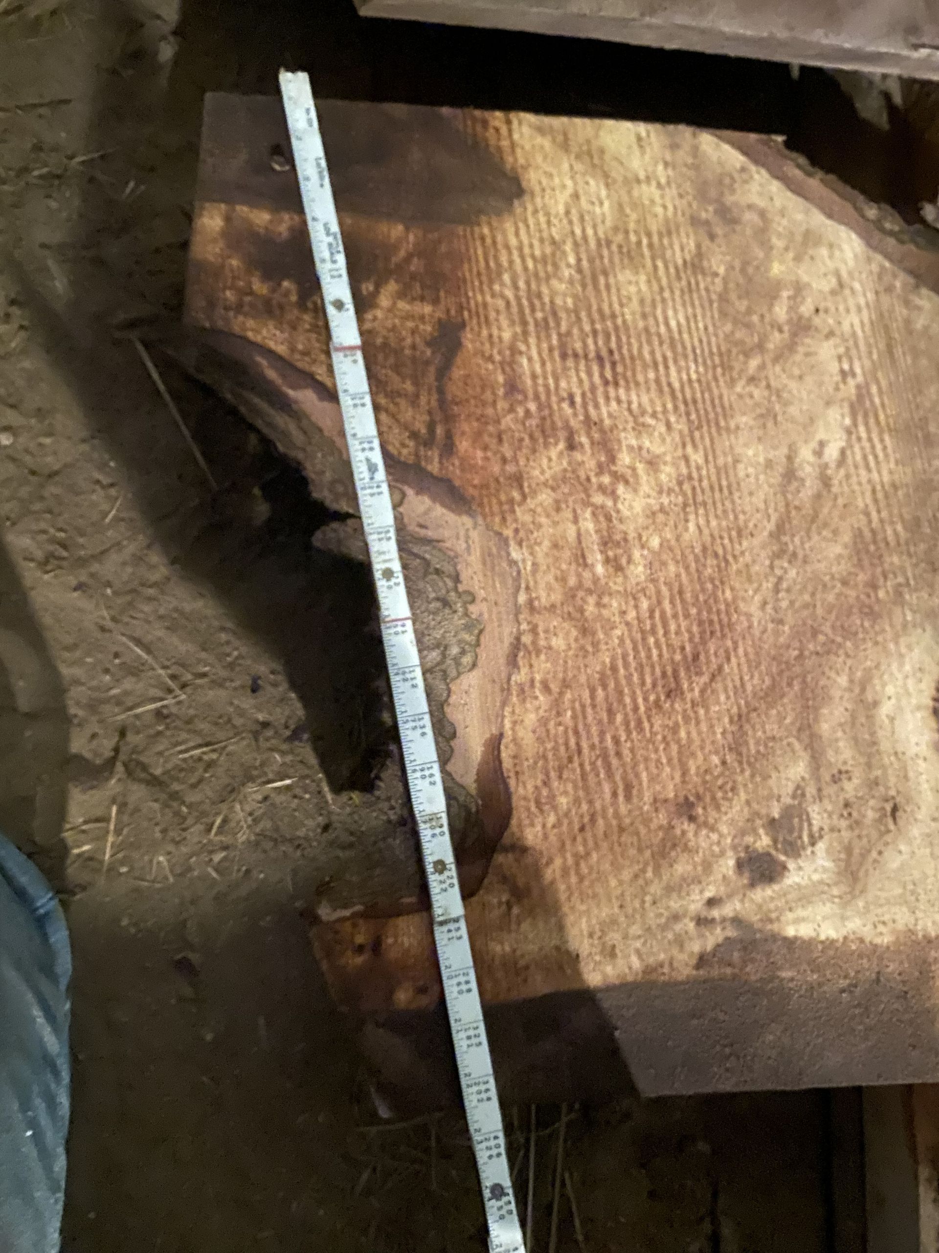 A wooden plank with a measuring tape laid across it, on a dirt floor.