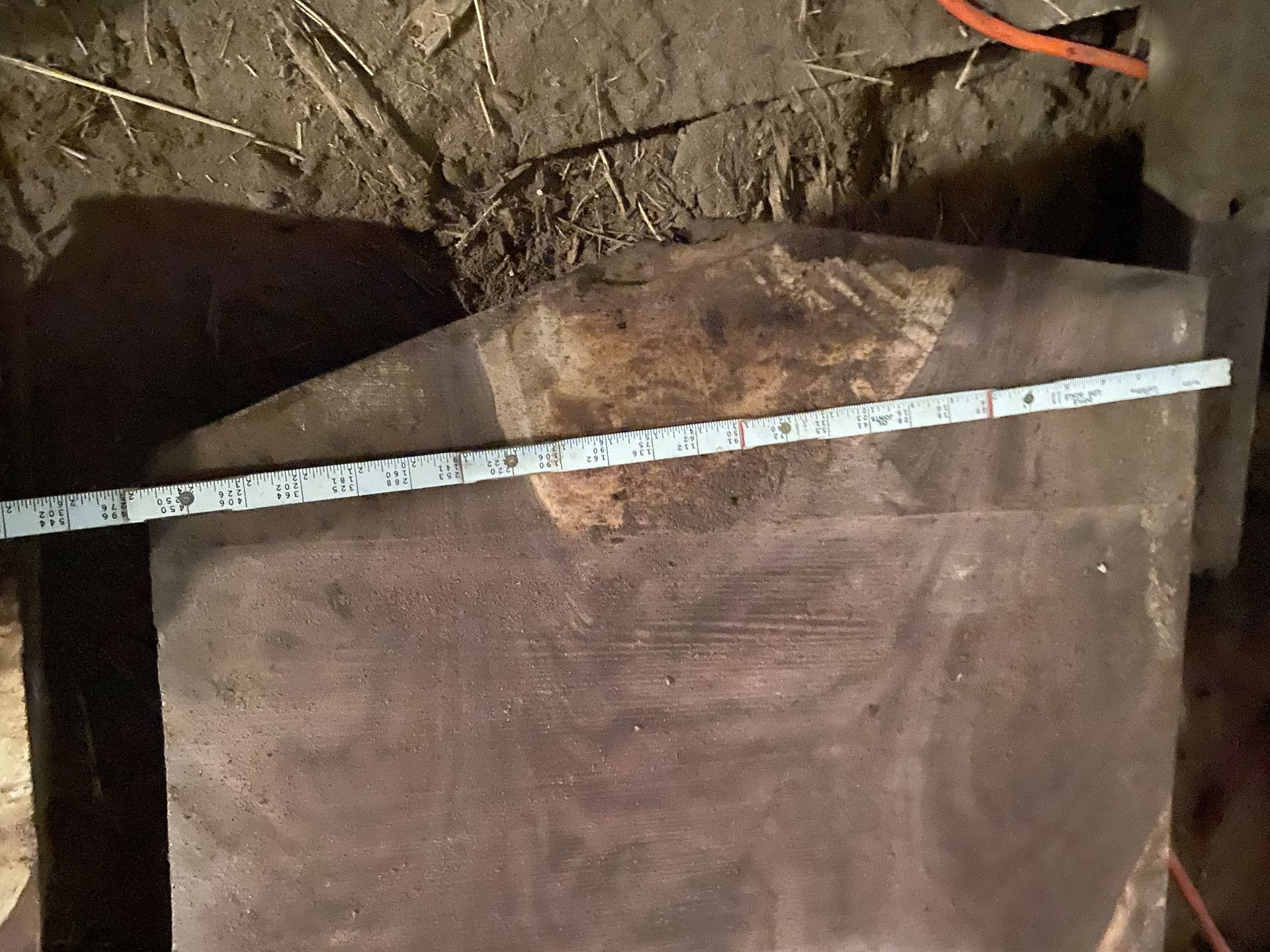 Dark, rectangular slab with a tape measure across it. The slab is weathered, likely metal.