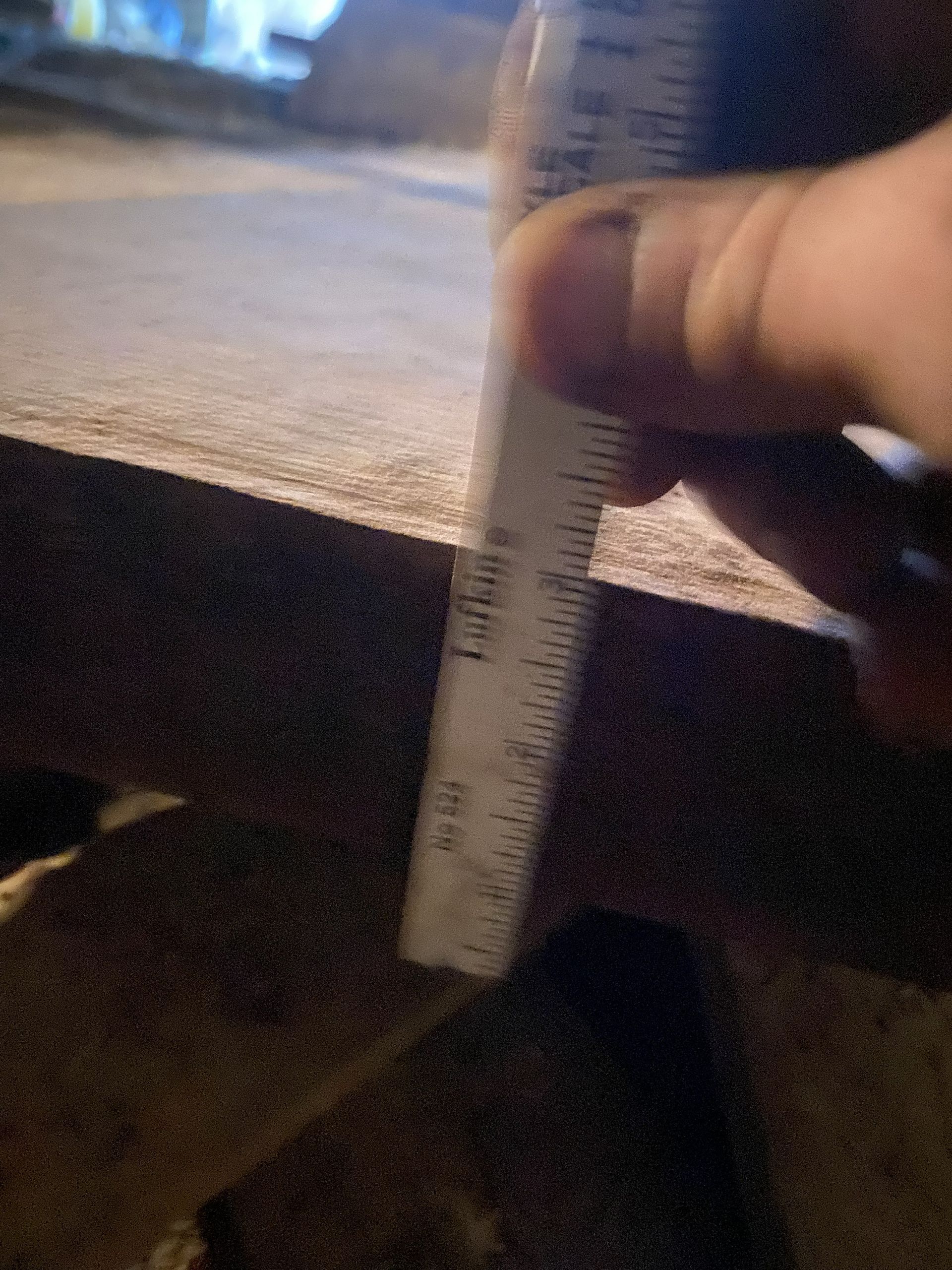 Hand holding a ruler, measuring a brown surface, likely a ledge or step, outdoors at night.