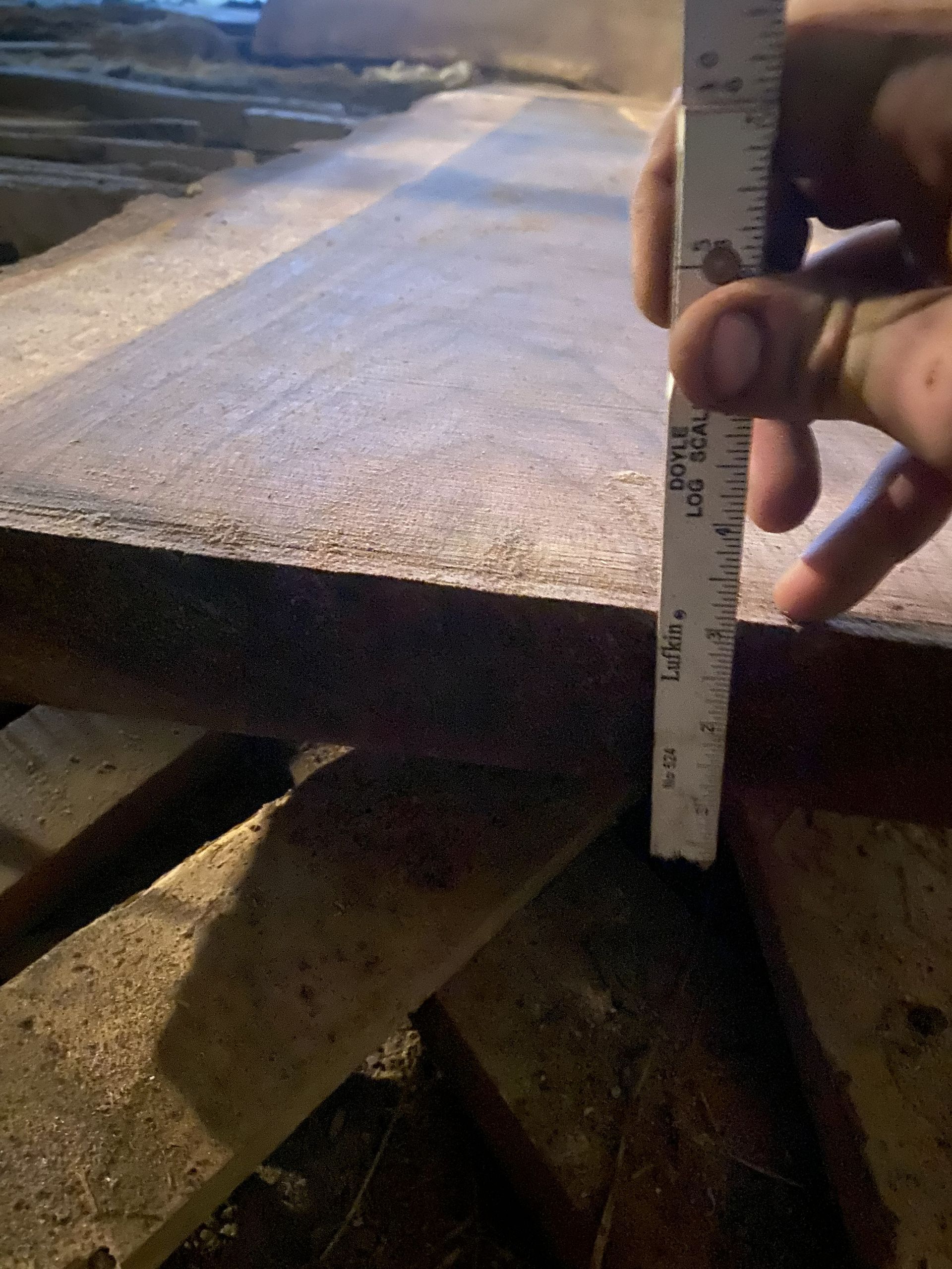 Hand measuring thickness of a wooden plank with a ruler in a dimly lit setting.