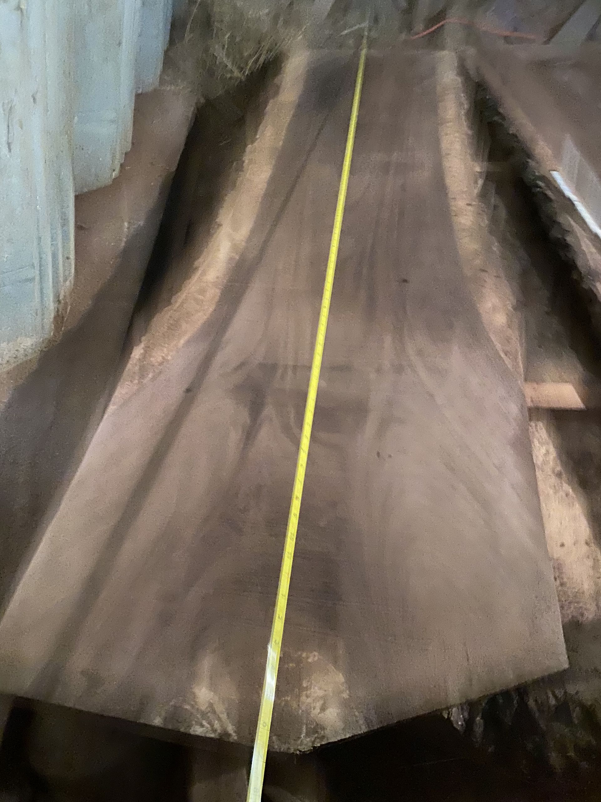 Large, dark-colored wood slab with yellow tape measure running down the center.