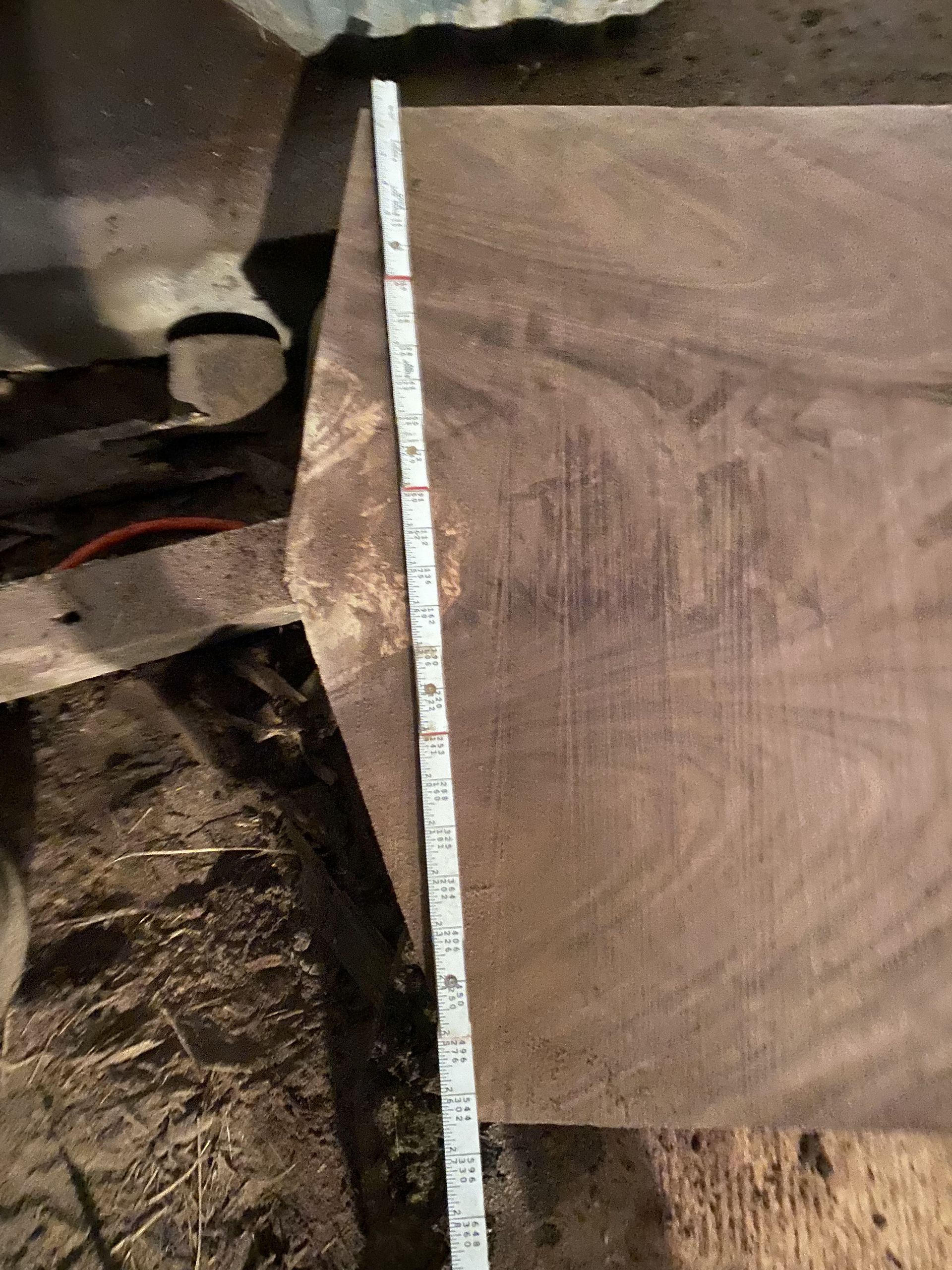 Tape measure against a dark wooden board, measuring its length in an indoor setting.