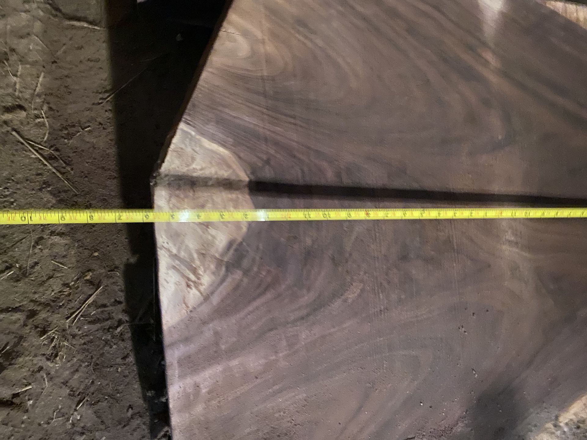 A dark wood slab with swirling grain, a yellow tape measure stretches across it, showing measurements.