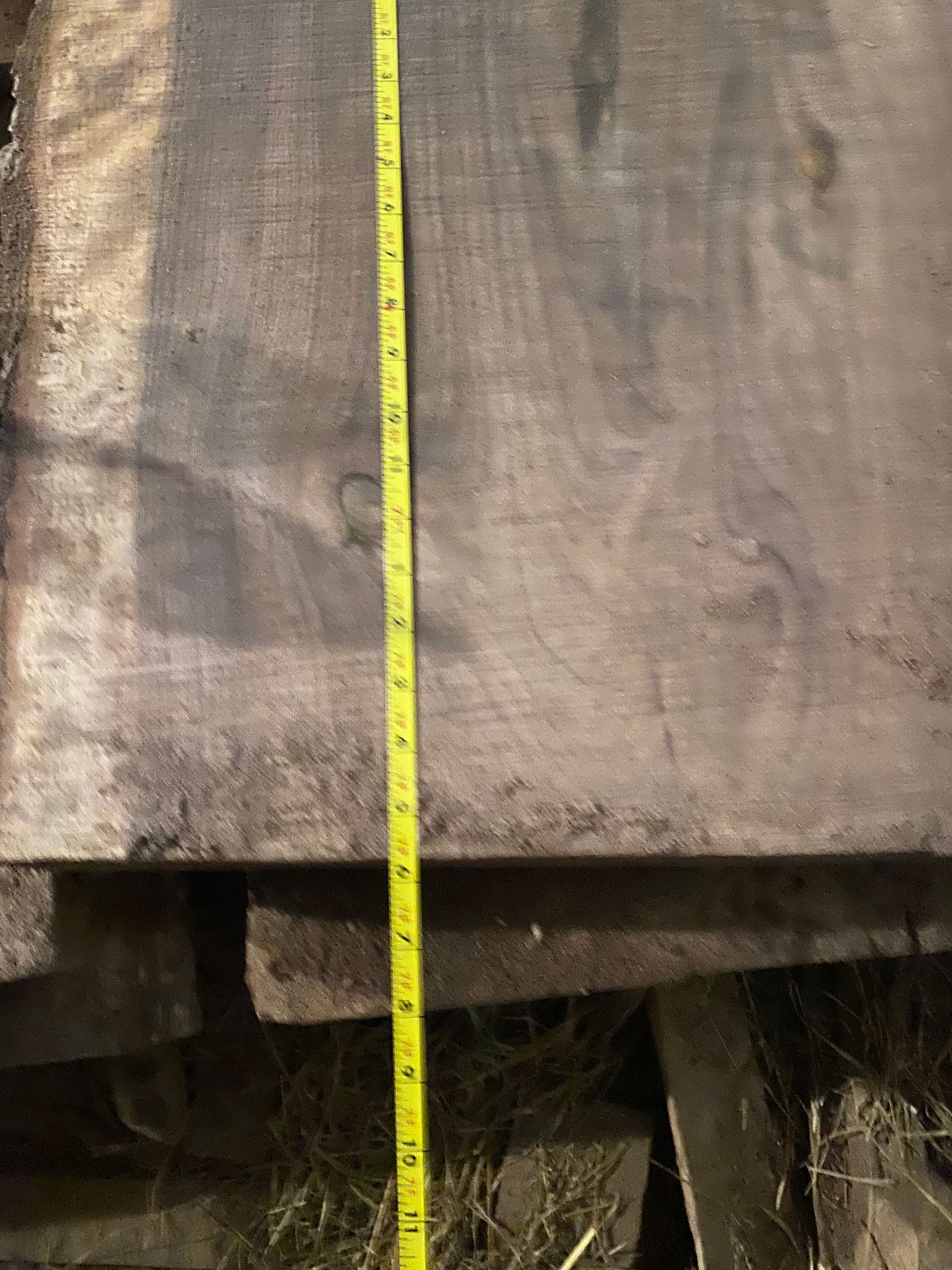 A dark wood slab with a yellow tape measure stretched vertically across it.