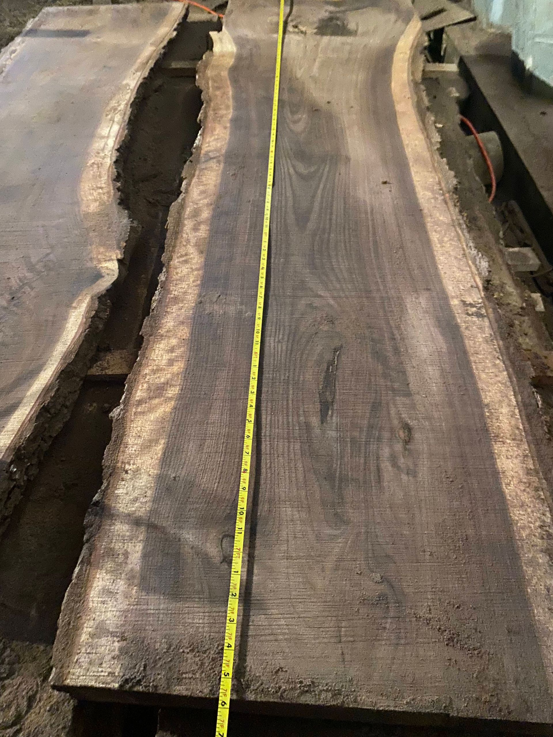 Two dark wood slabs with live edges, a yellow tape measure laid lengthwise.
