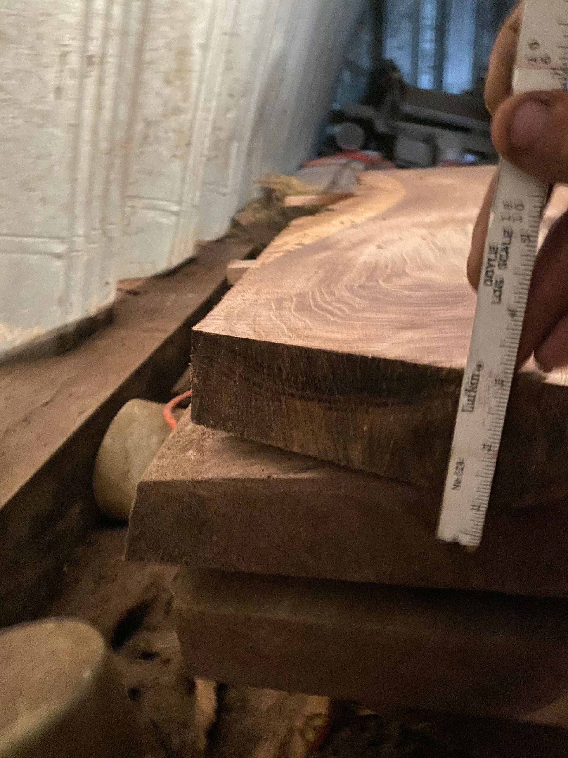 Measuring the thickness of stacked wooden planks with a ruler in a dim, rustic setting.