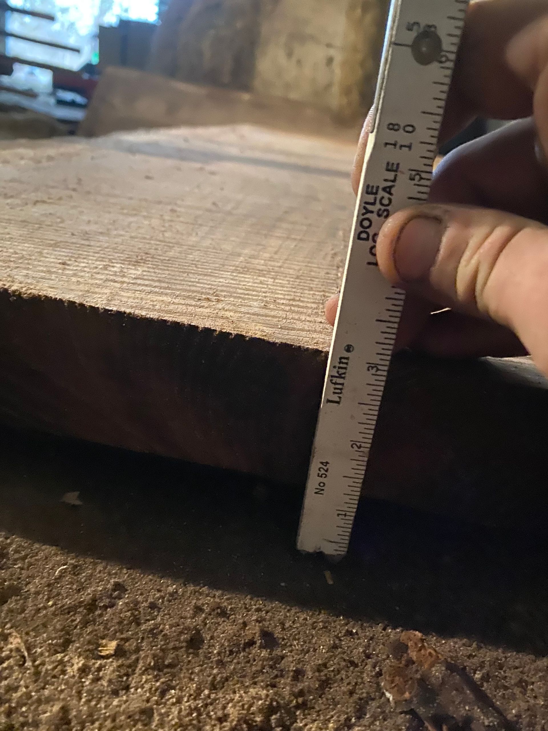 Hand measuring the thickness of a wooden board with a ruler.