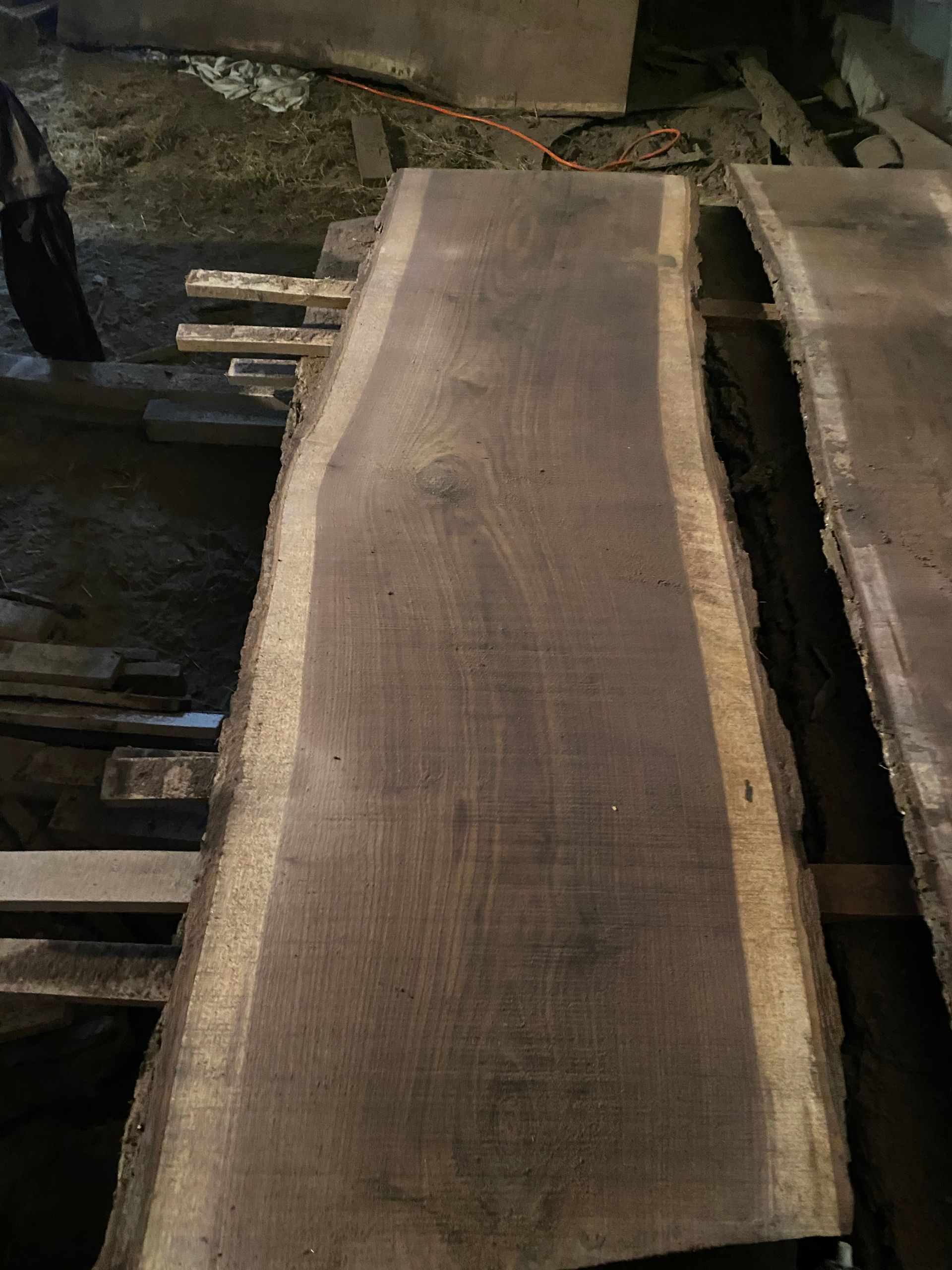 Dark wood slab with live edge, lying in a dimly lit space.