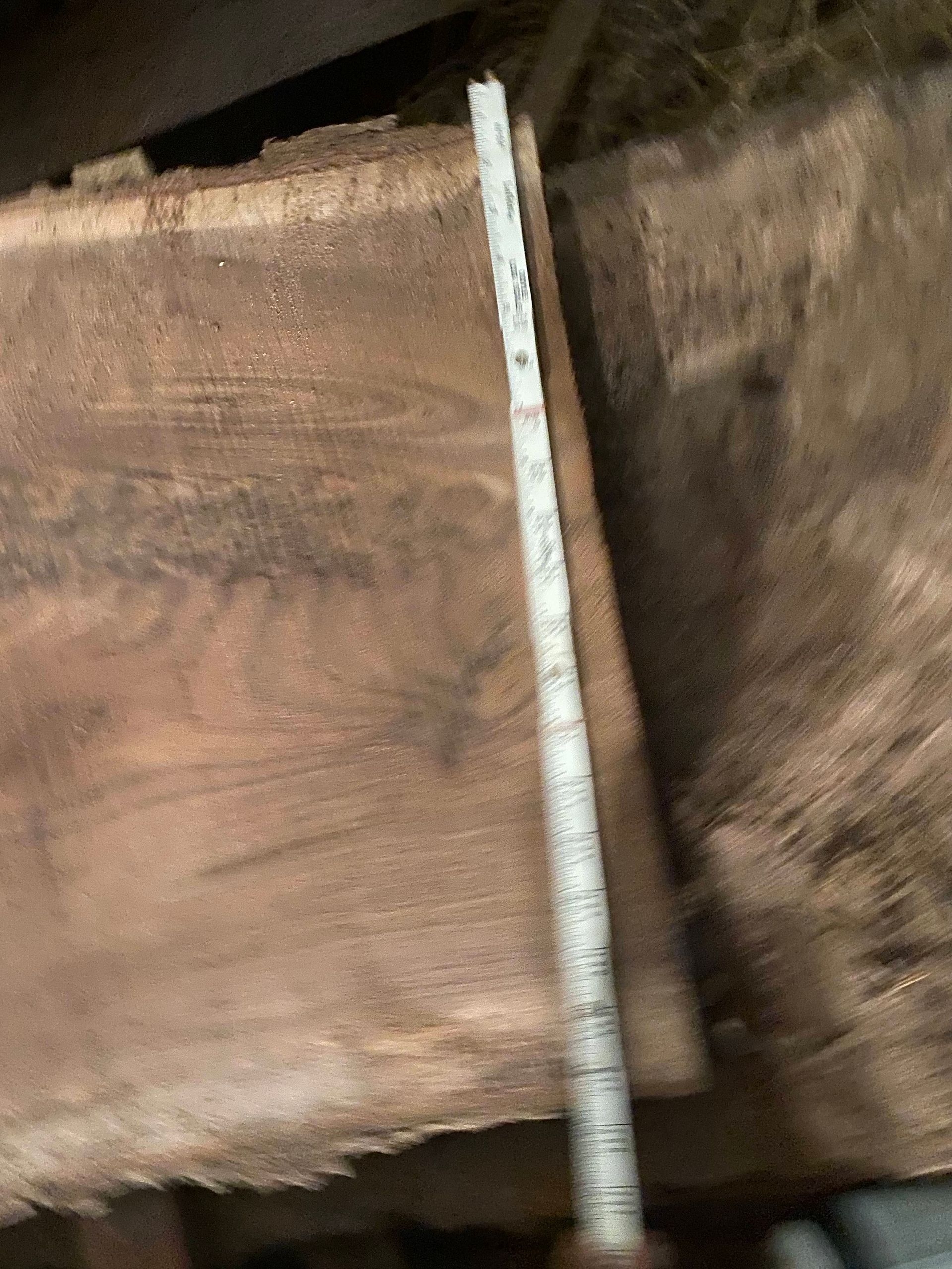 A measuring tape next to a thick, rough-edged piece of wood, possibly a slab, indoors.