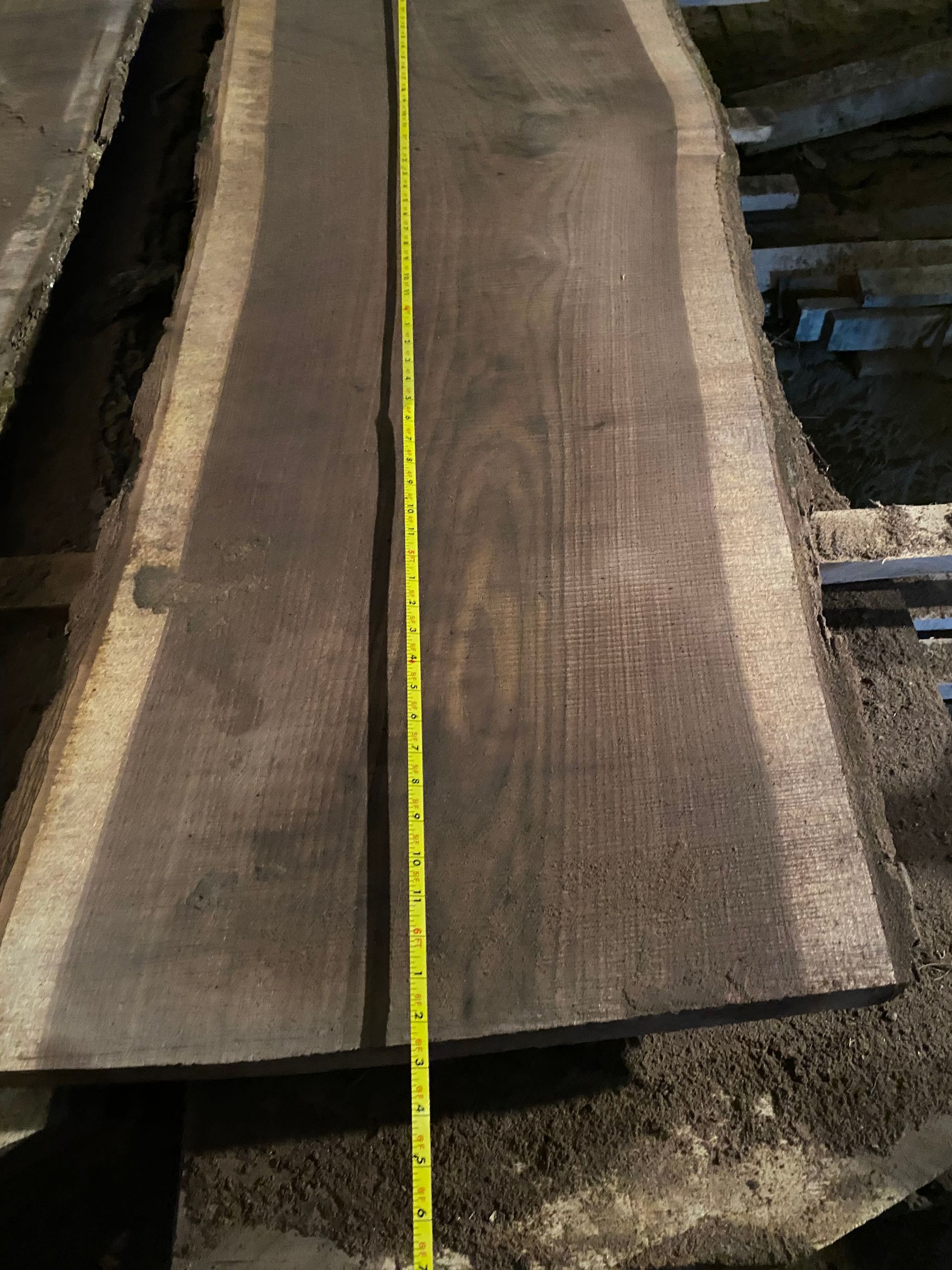 Dark wood slab with a yellow tape measure, likely in a lumber yard.