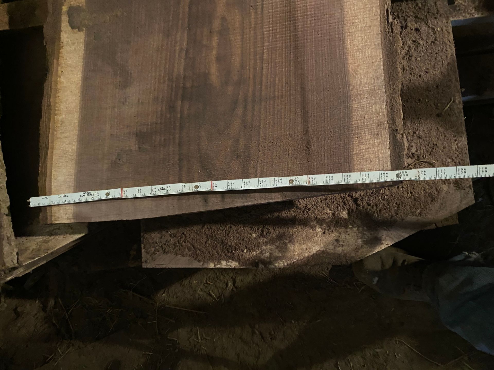 Dark wood slab with a ruler laid across it, resting on a dusty surface.