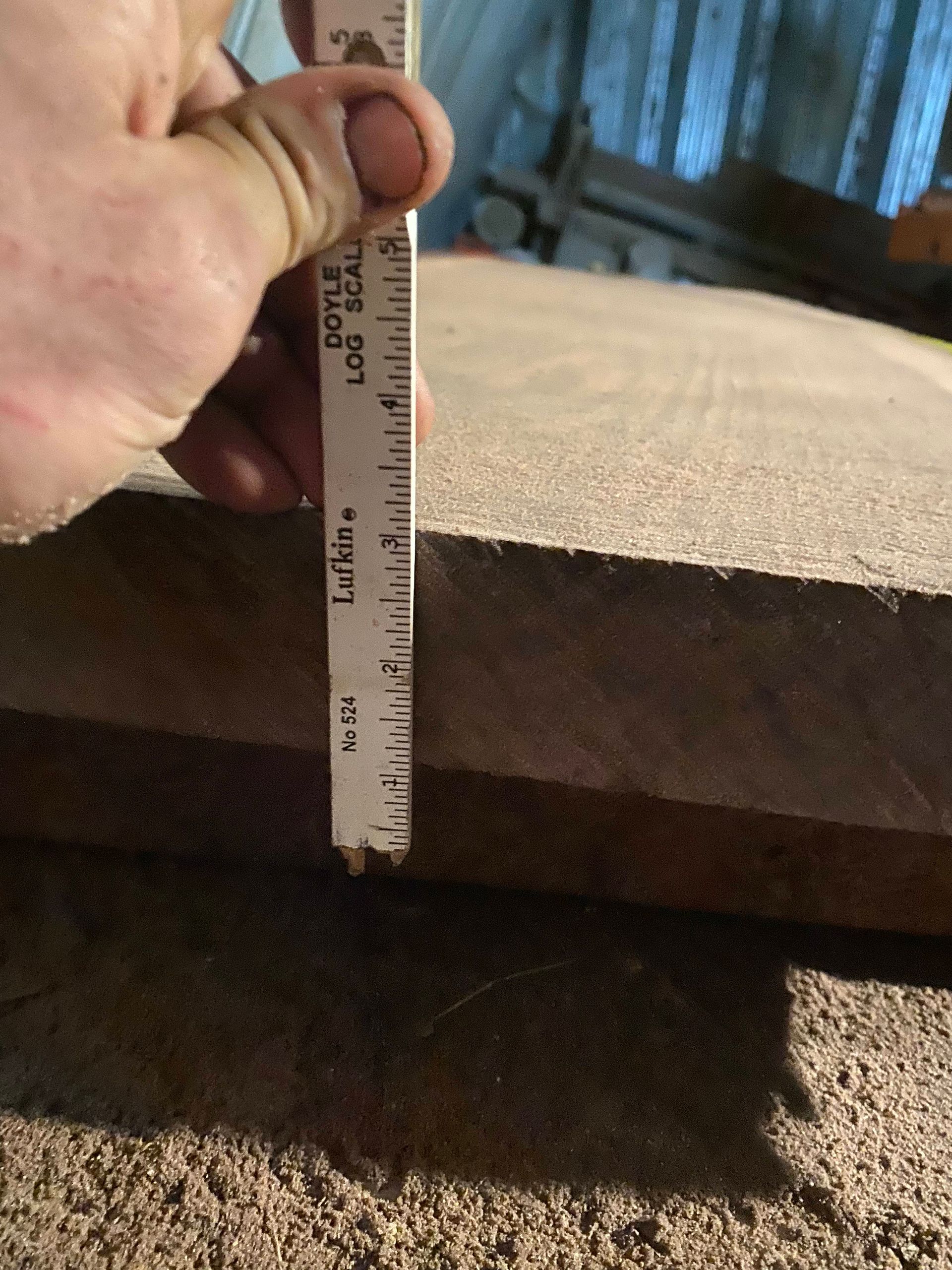 Hand holding a ruler, measuring the thickness of a wooden board, in a workshop setting.