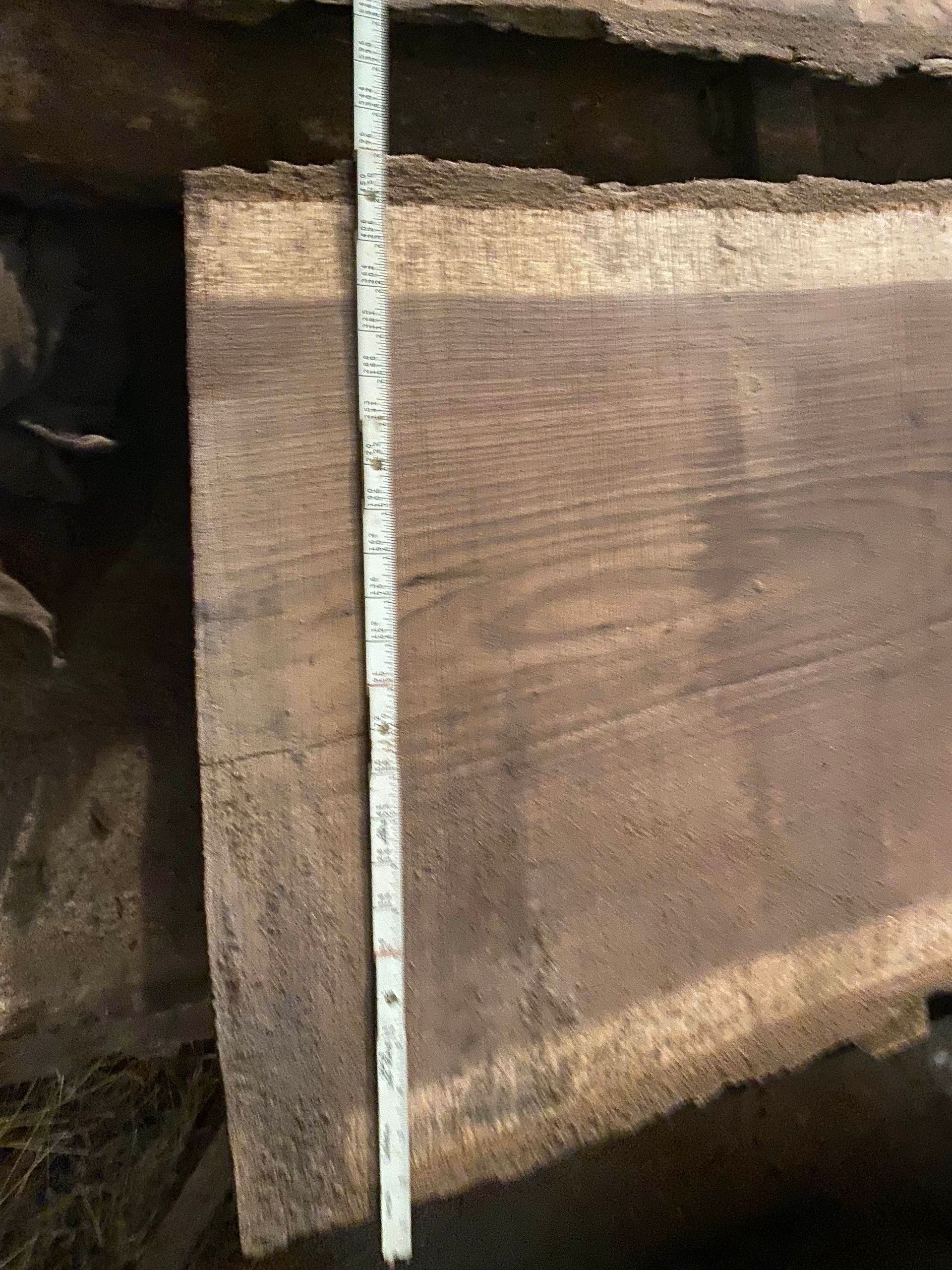 Wooden slab with live edge, brown with visible wood grain, measuring tape alongside.