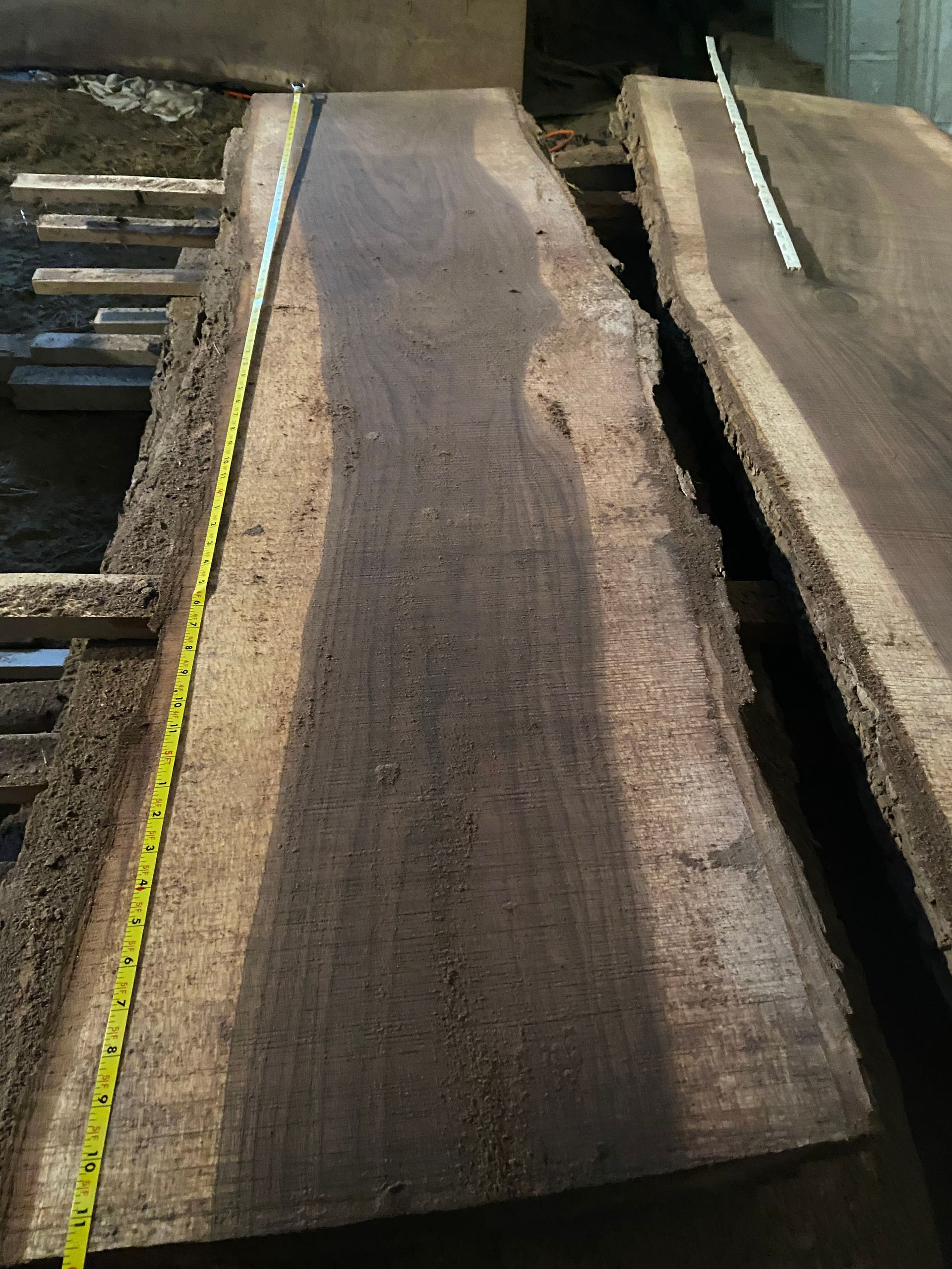 Two dark-colored wood slabs with live edges, a yellow tape measure laid across the first slab.