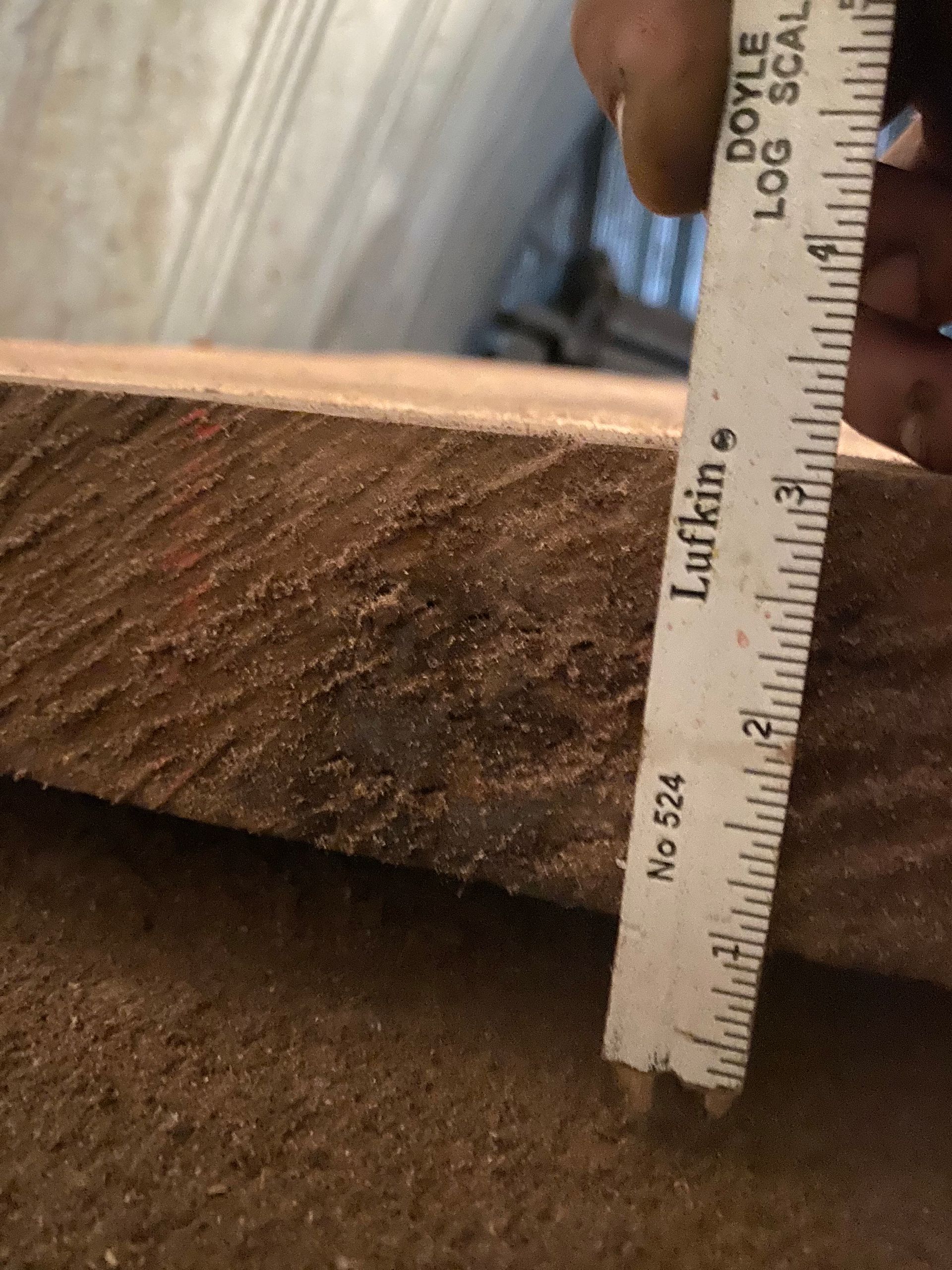 Person measuring the thickness of a wood plank with a Lufkin ruler; showing about 1 1/2 inches.