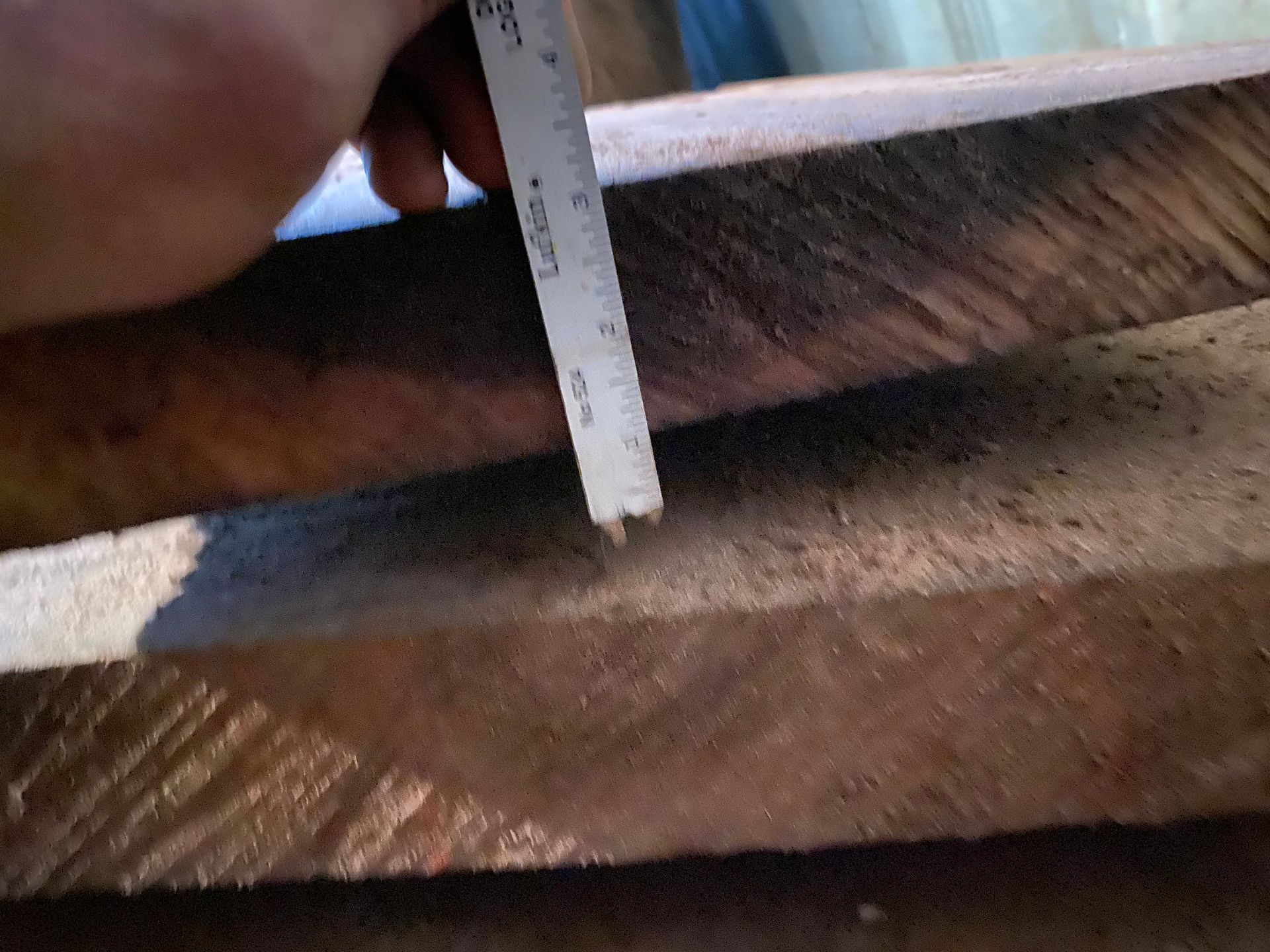 Hand holding ruler measuring the thickness of wooden planks.