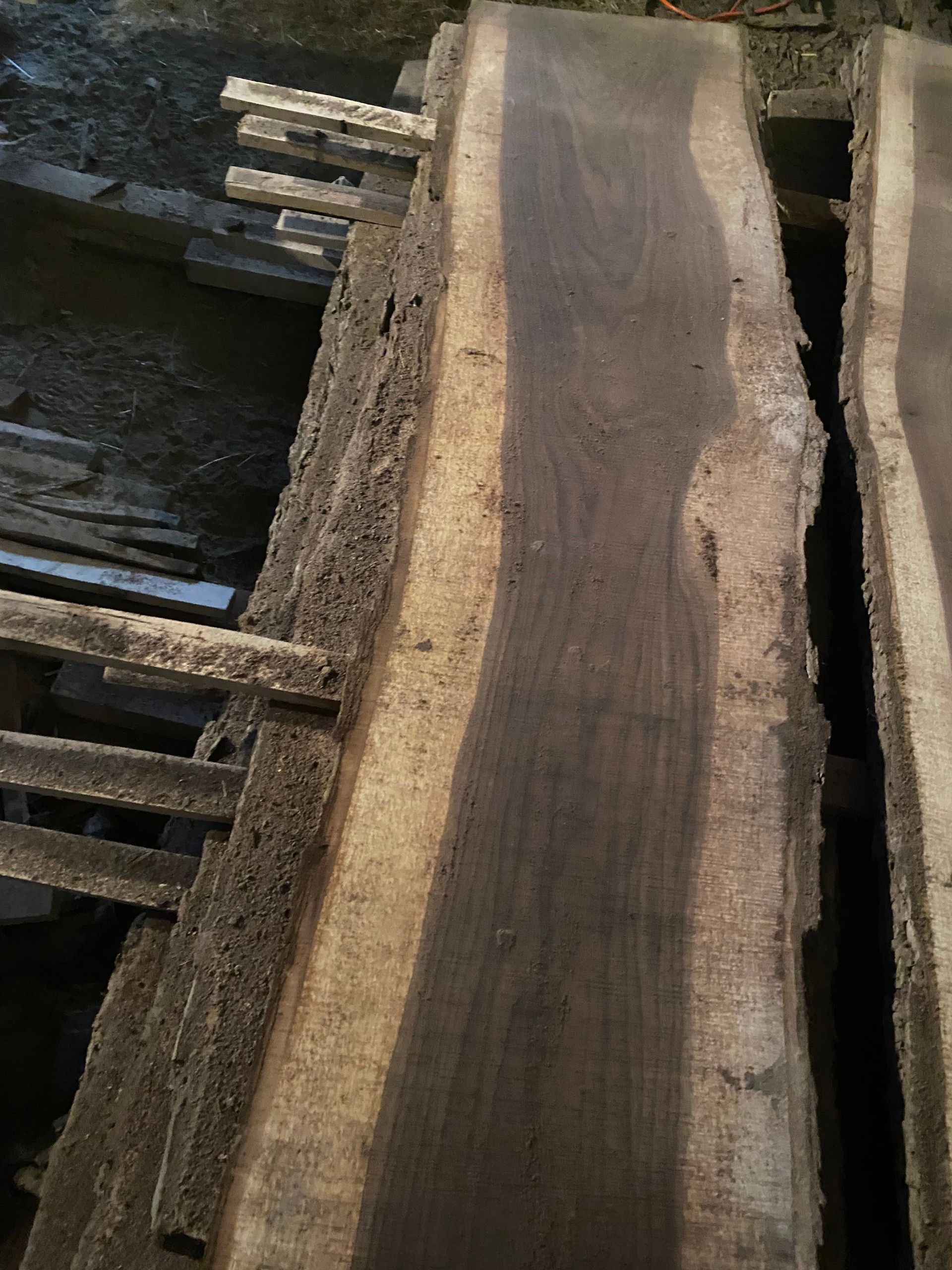 Stack of dark wood planks with lighter edges, outdoors.