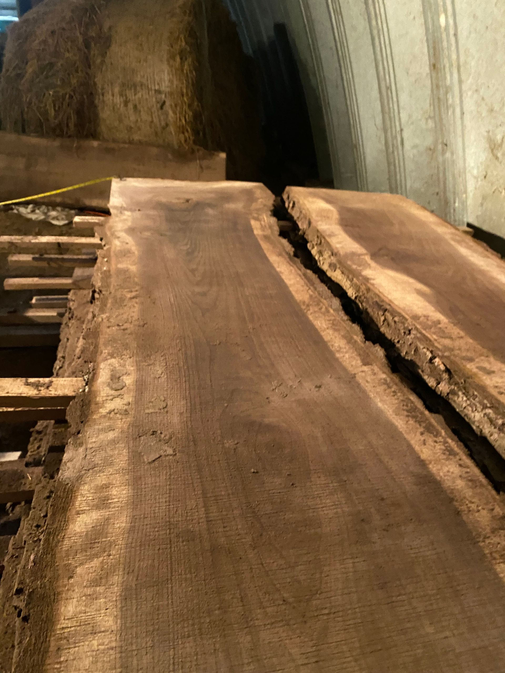 Raw, dark wood slabs stacked, possibly for furniture, inside a dimly lit structure.