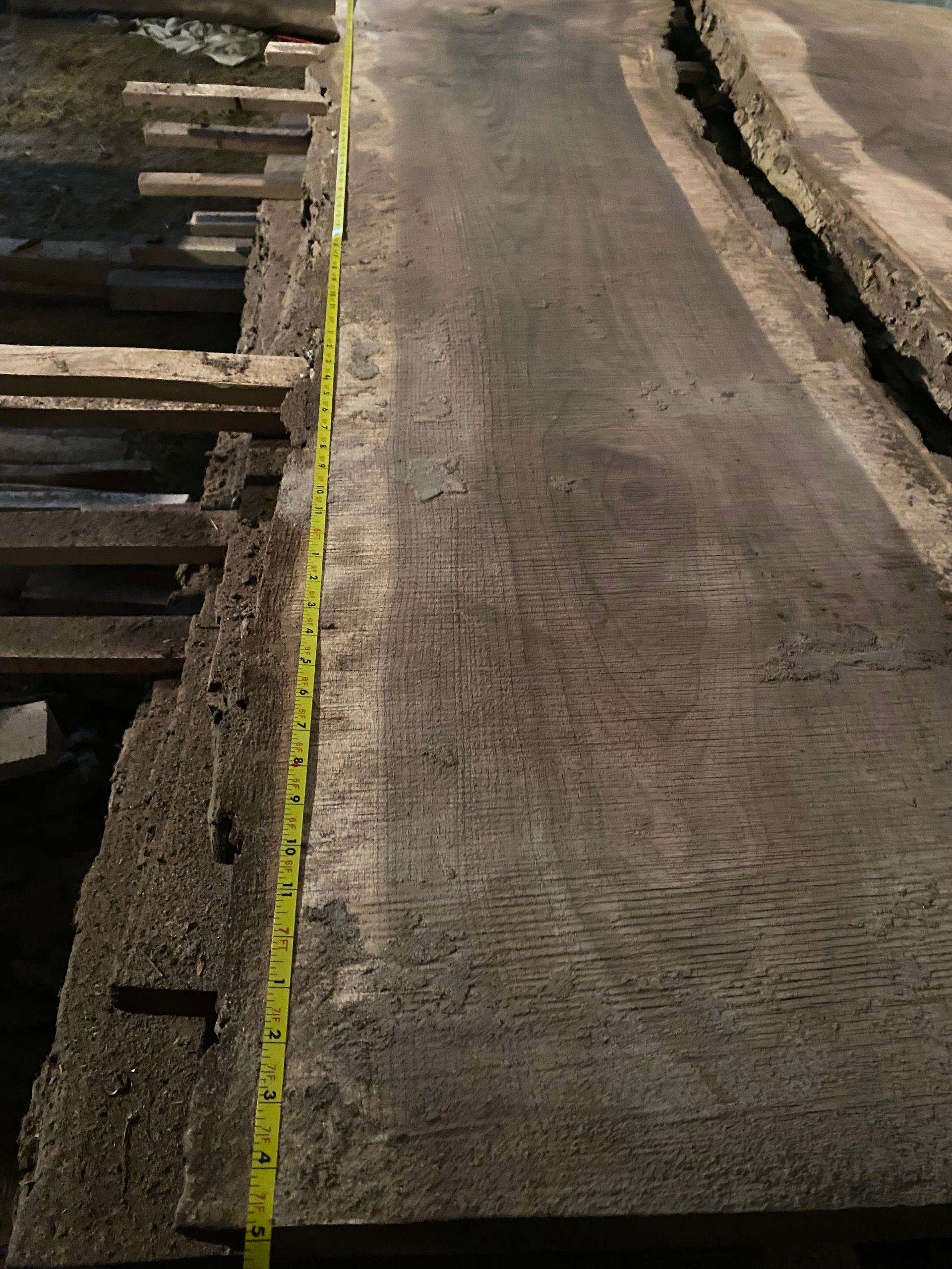 A large, dark wooden plank with a yellow tape measure running its length.