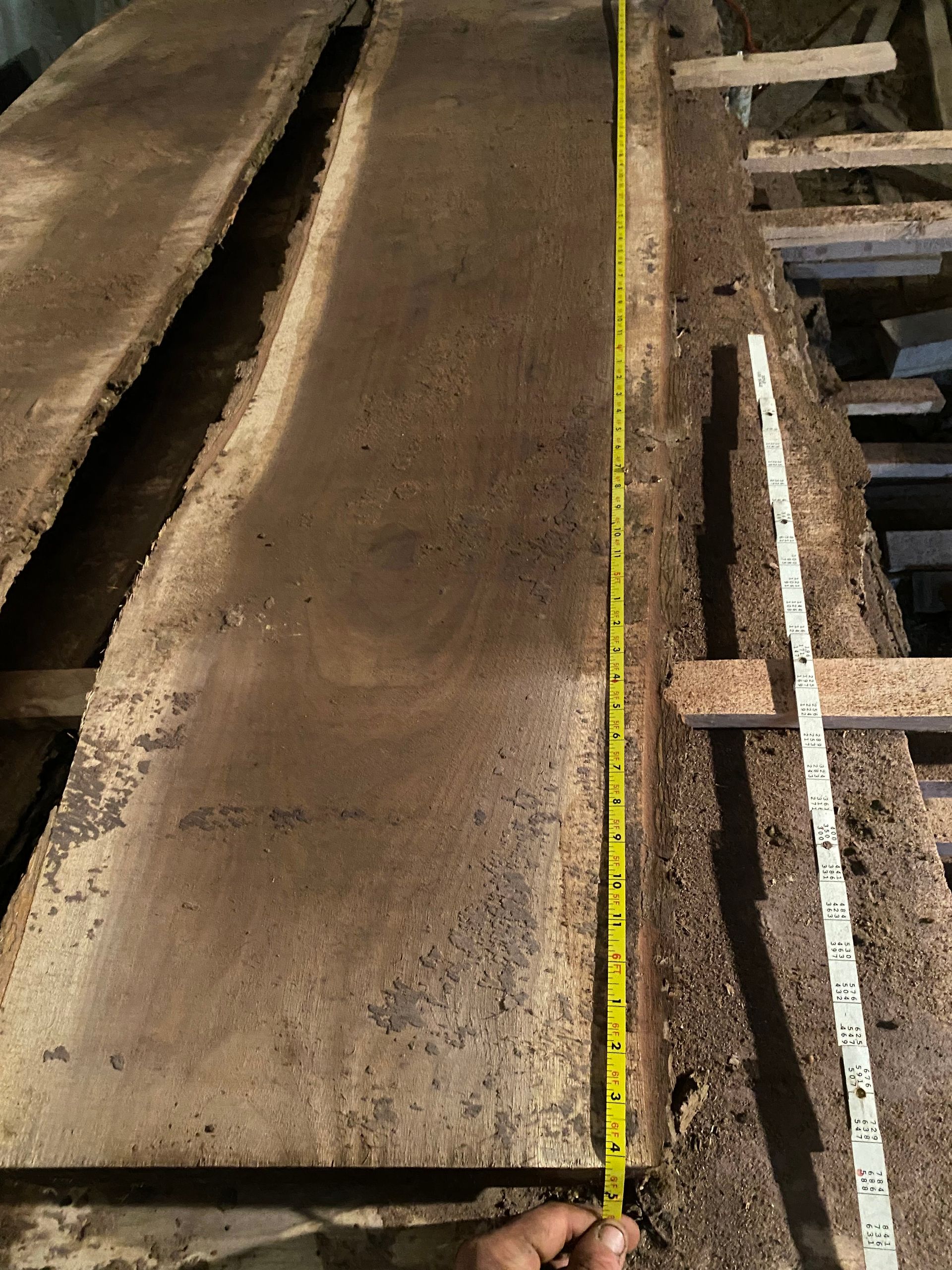 Two rough-sawn wood planks, one with a yellow tape measure, and a white ruler on a rough wooden surface.