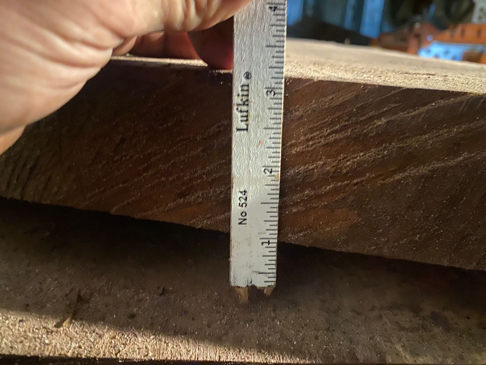 Hand holding a ruler measuring the thickness of a wooden plank.