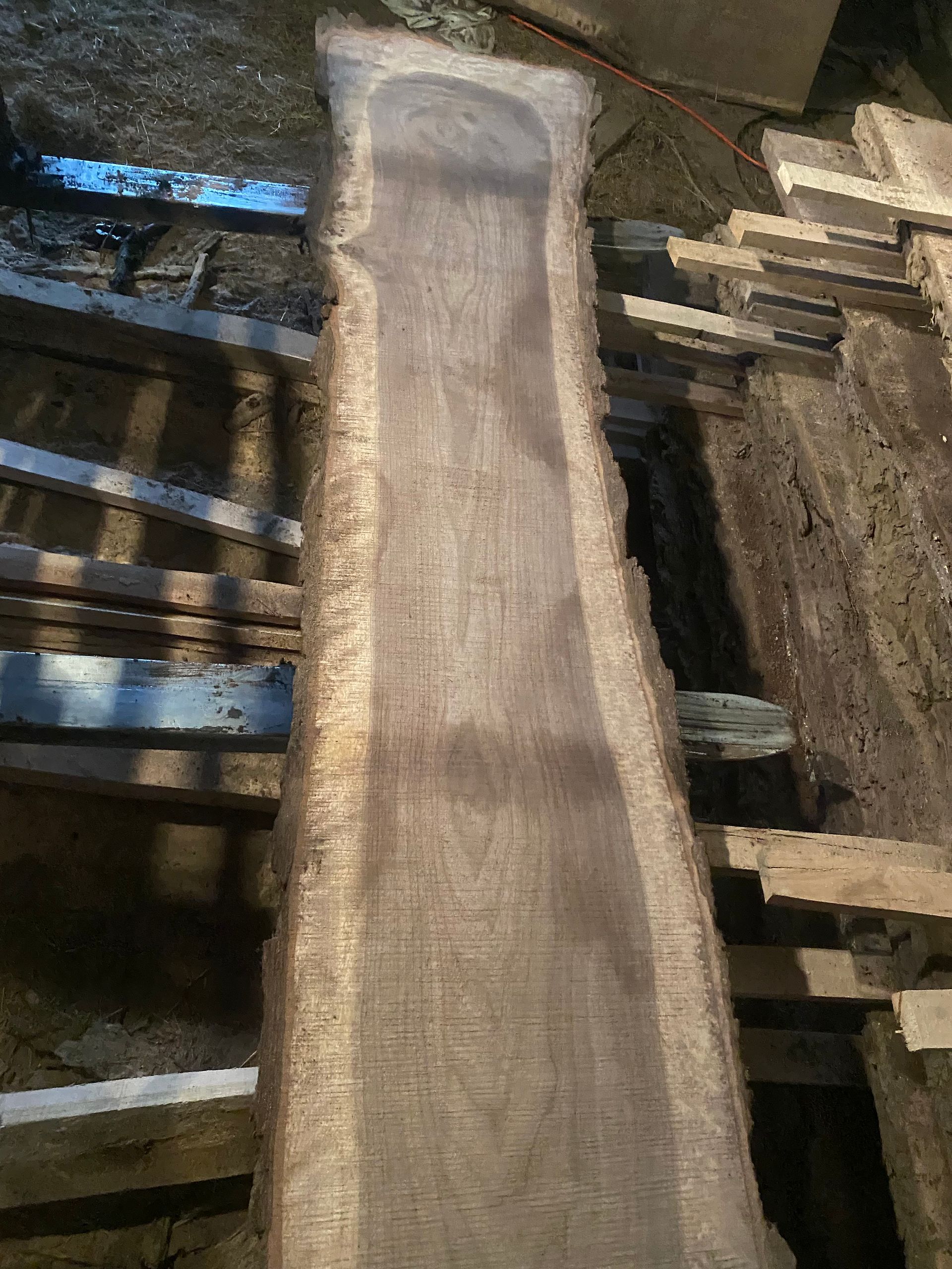 Long, rough-edged wooden slab, possibly a table top, in a workshop setting.