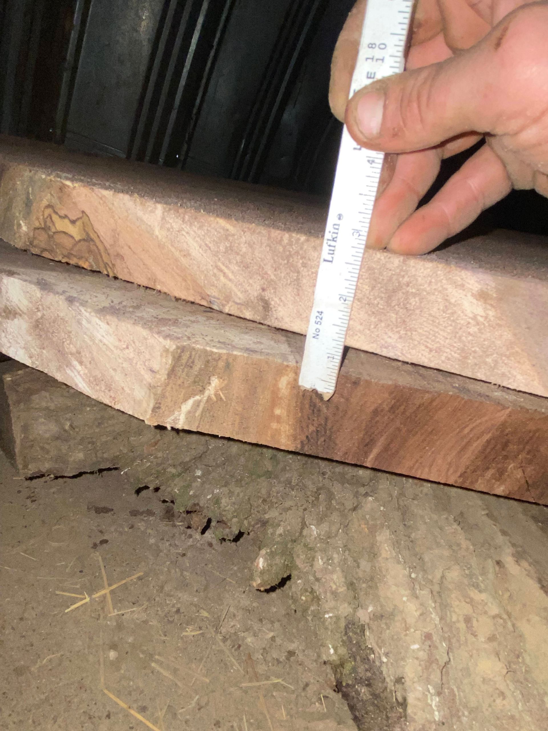 Person measuring the thickness of two wooden planks with a ruler.