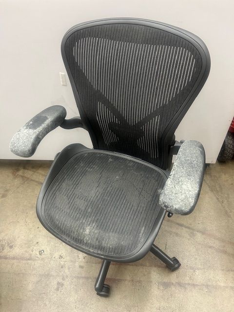 A black office chair with a broken arm rest is sitting on the floor.