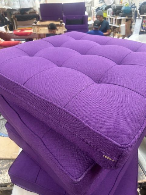 Purple cushions are stacked on top of each other in a factory.