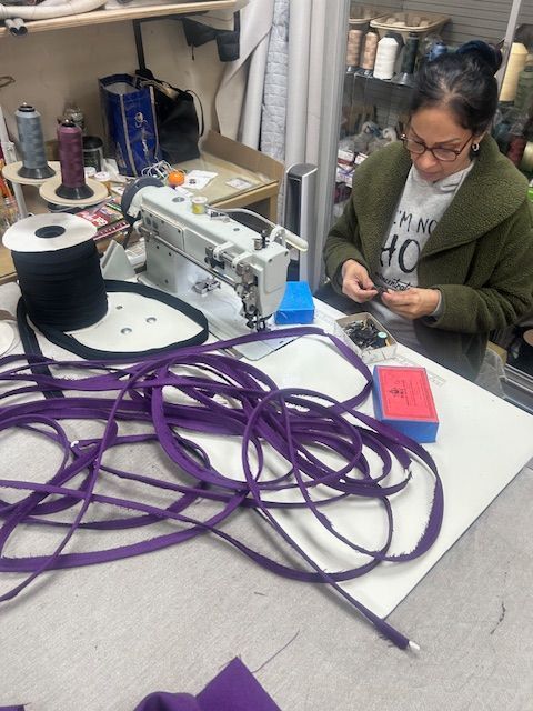 A woman sitting at a table with a sewing machine and purple ribbons