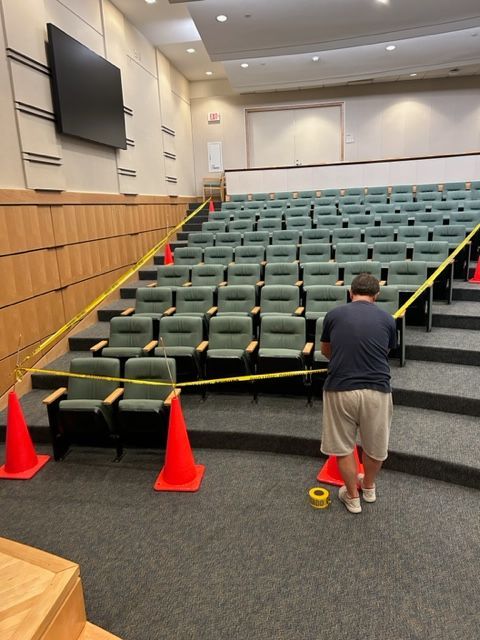 A man is standing in an auditorium with orange cones and yellow tape