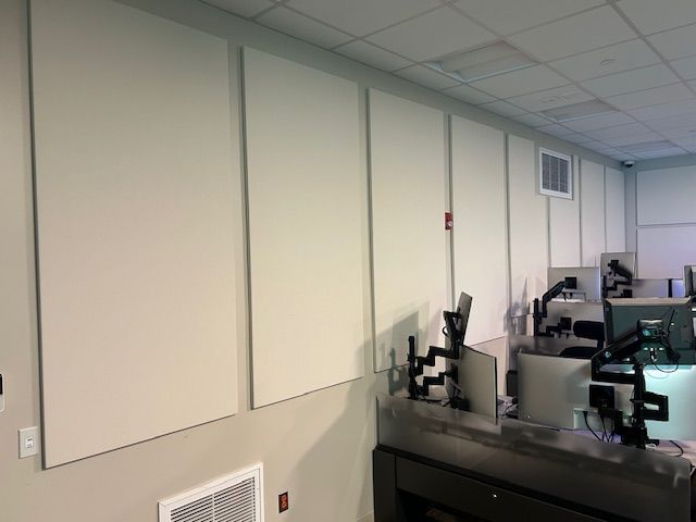 White sound-absorbing panels on a wall in an office setting with computer monitors and desks.