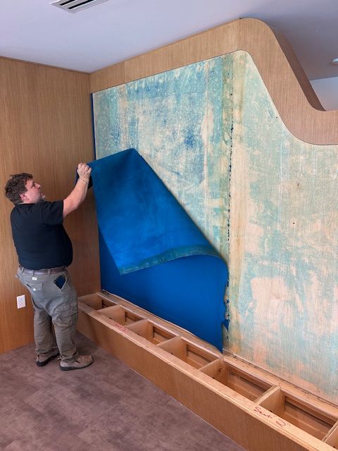 Person removing blue fabric from wall panel. Wooden structure, light brown wood, room setting.