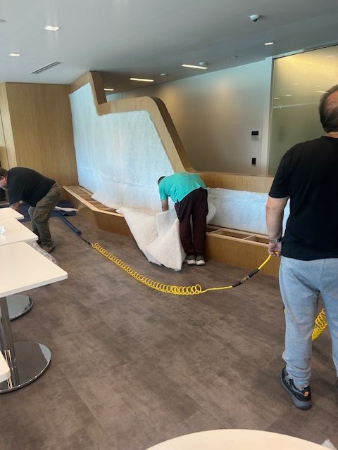 Three people installing a white fabric covering on a built-in seating area. Yellow caution tape is on the floor.