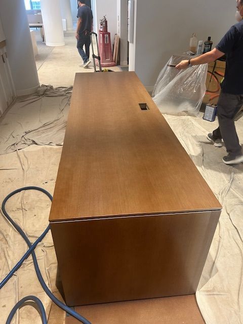 A dining room table is being painted in a room with a chandelier.
