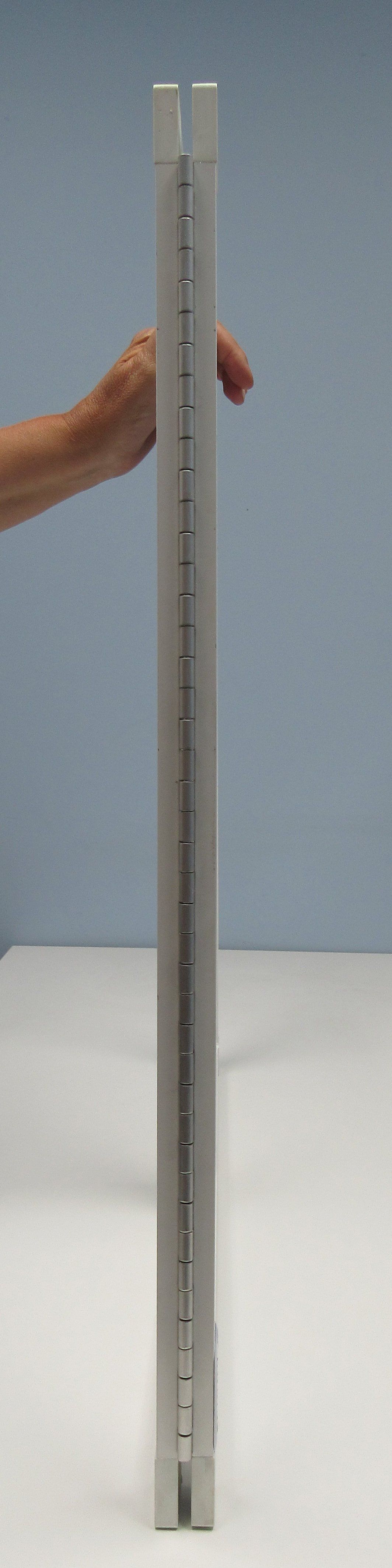 A person is holding a pencil over a metal tube on a table.
