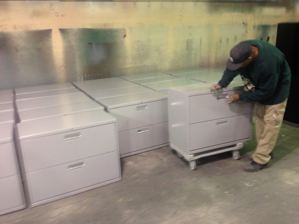 A man is painting a row of filing cabinets in a room.