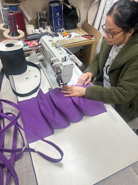 A woman is using a sewing machine to sew purple fabric