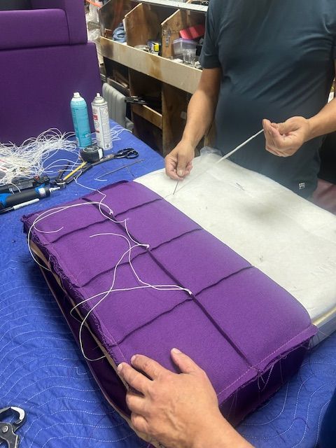 Two people are working on a purple cushion on a table