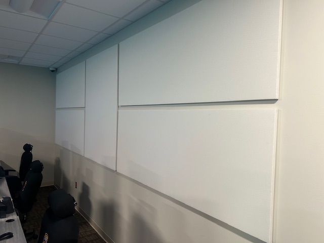 White panels on a wall in a room. Some black chairs are in the corner.