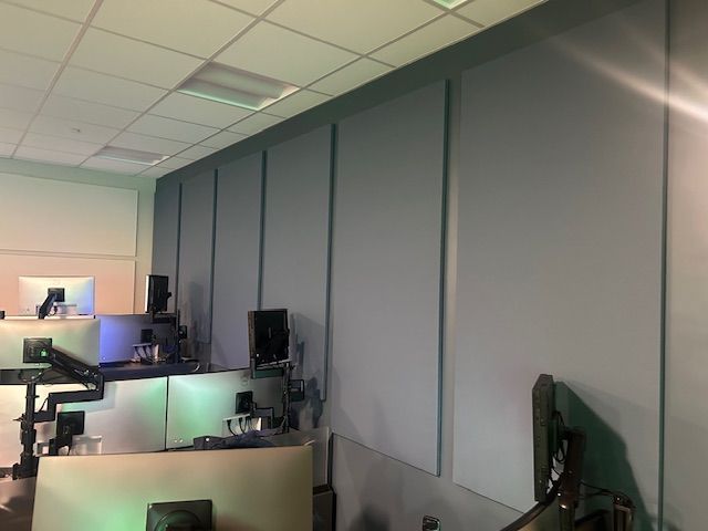 A room with sound-dampening panels on the wall, computer workstations in foreground.